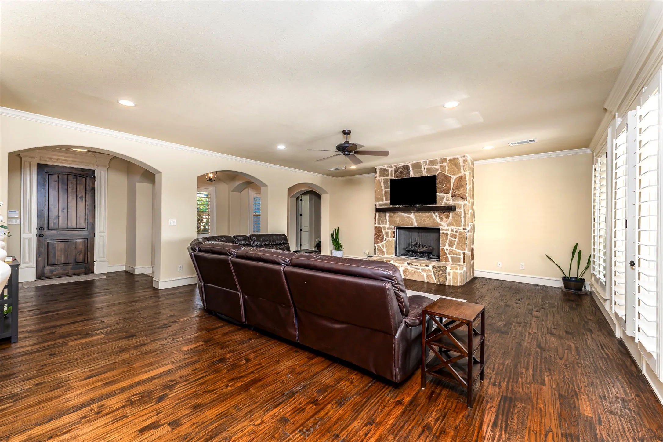 Stone-clad fireplace with mantel, dark wood-finish flooring, recessed lighting, and white plantation shutters