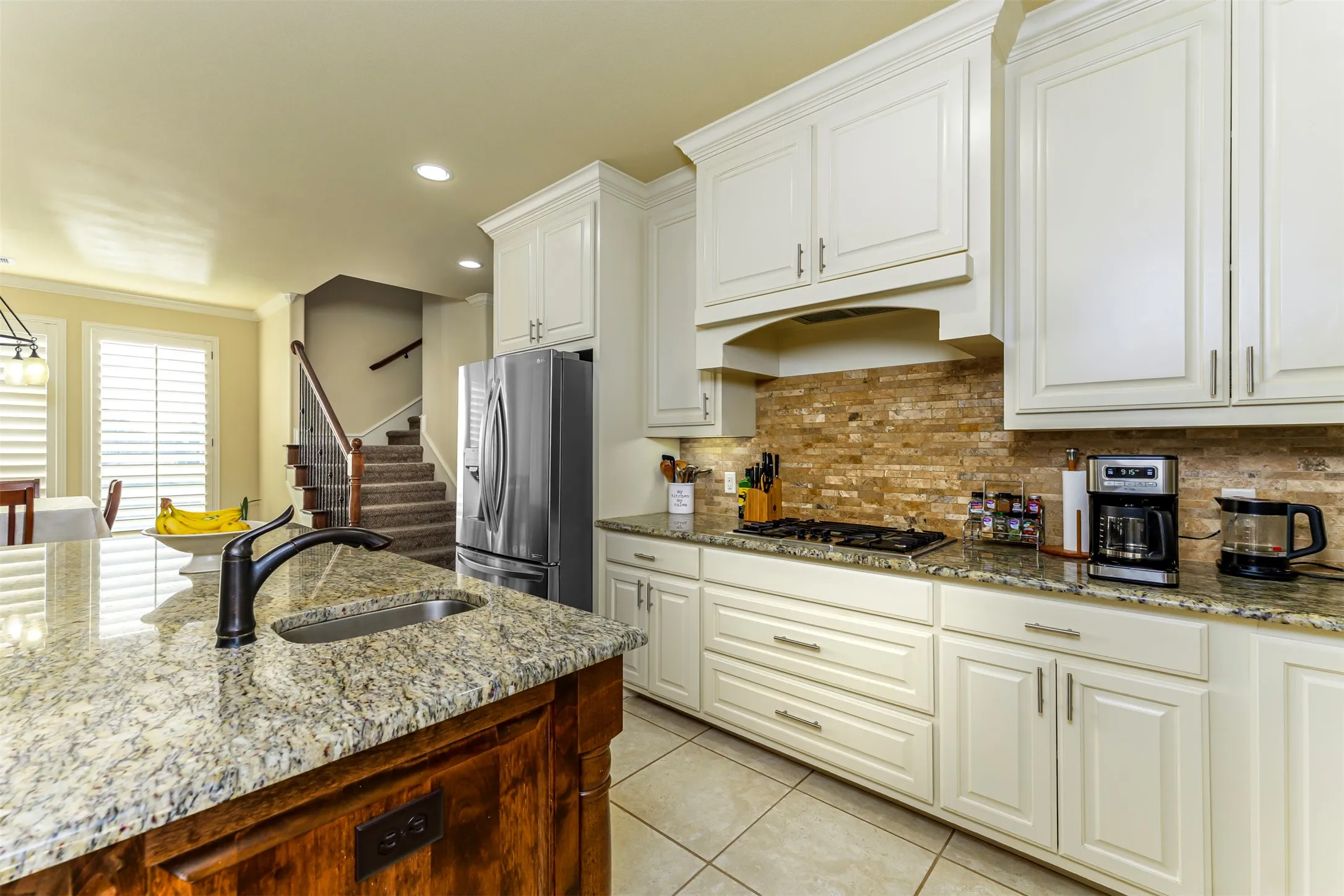 Kitchen featuring a large island with an undermount sink, granite countertops, white cabinetry, a stone tile backsplash, and tile flooring