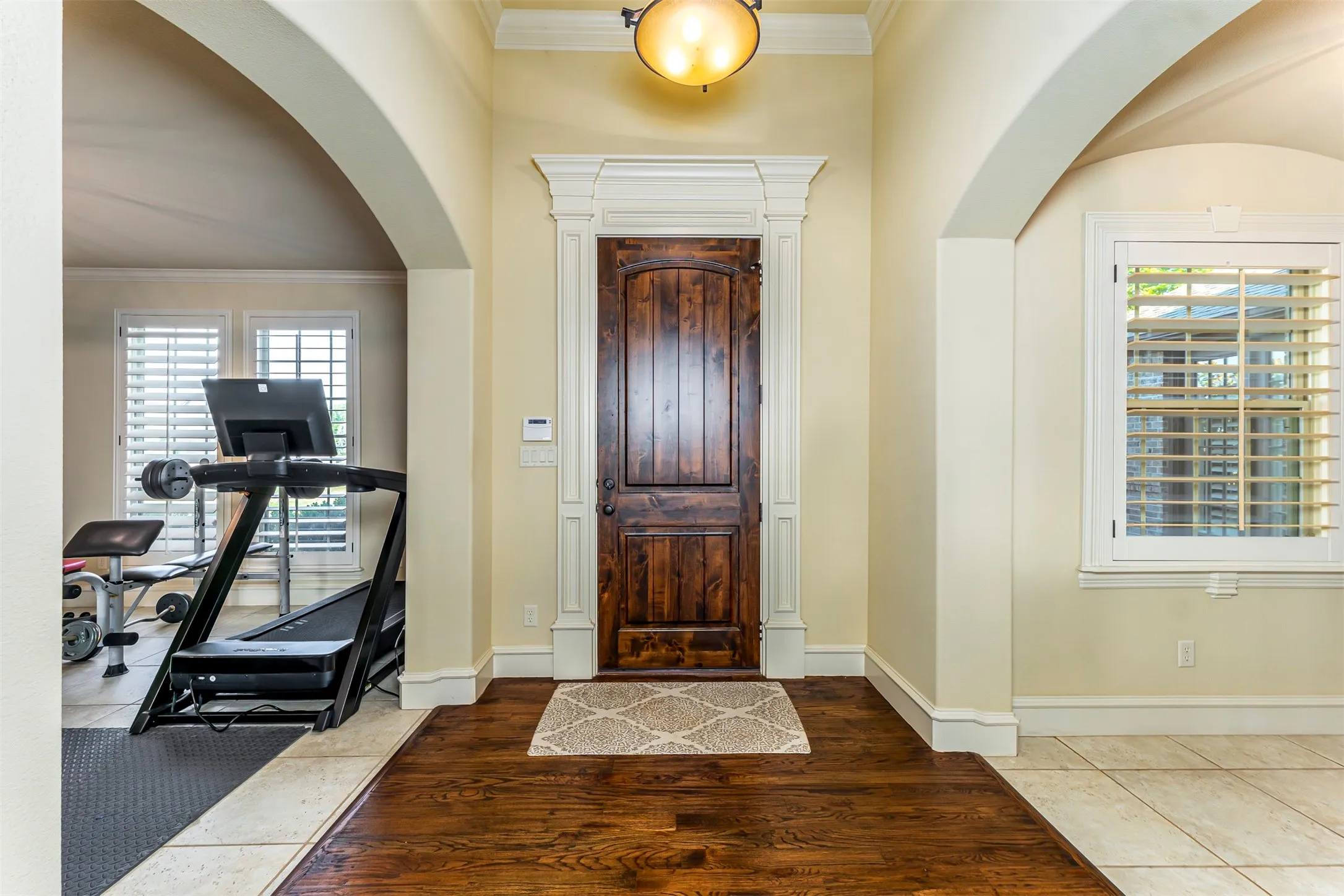 Hardwood flooring, arched doorways, a paneled wooden door with decorative trim, and crown molding