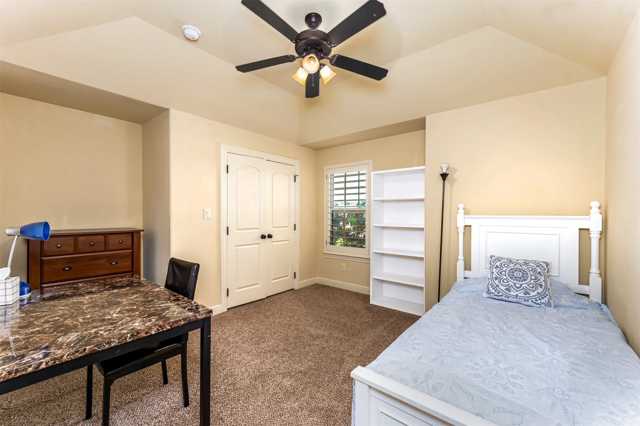 Vaulted ceiling with a ceiling fan, carpeted flooring, window with plantation shutters, double-door closet, and built-in shelving