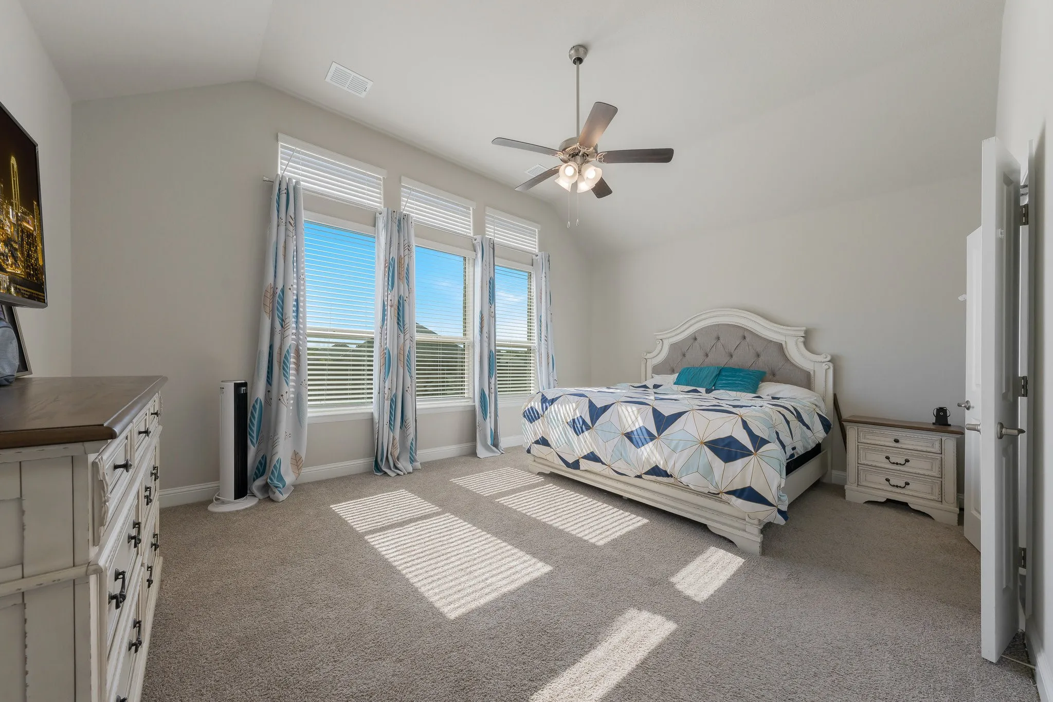 Spacious primary bedroom with lofted ceiling, light colored carpet, lot of light and a ceiling fan