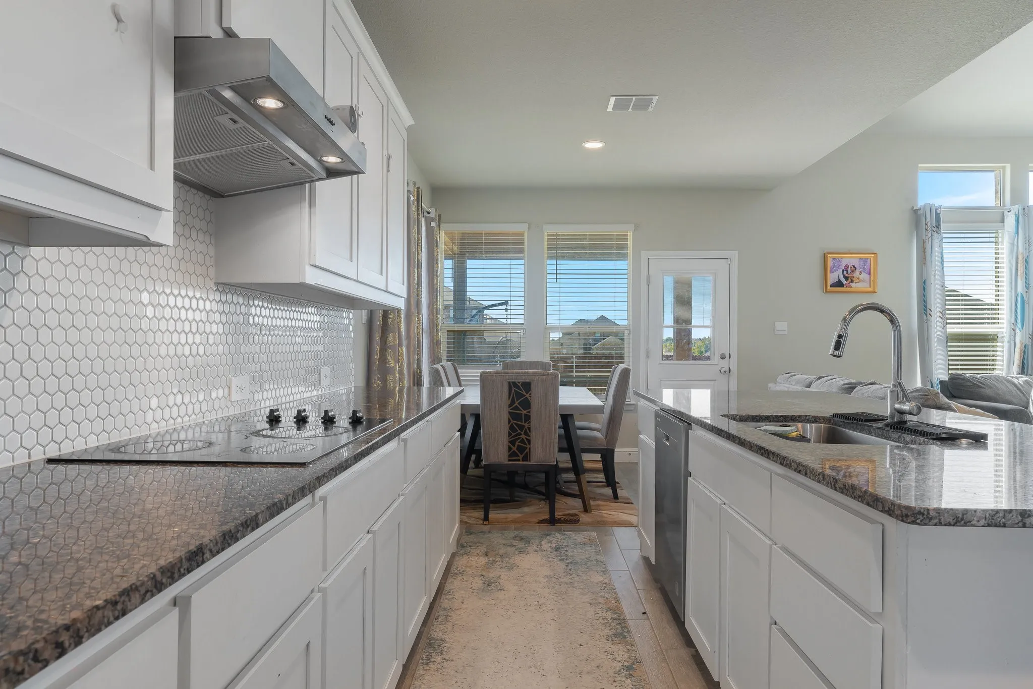 Kitchen with white cabinets, tasteful backsplash, range hood, dark stone countertops, and an island with sink