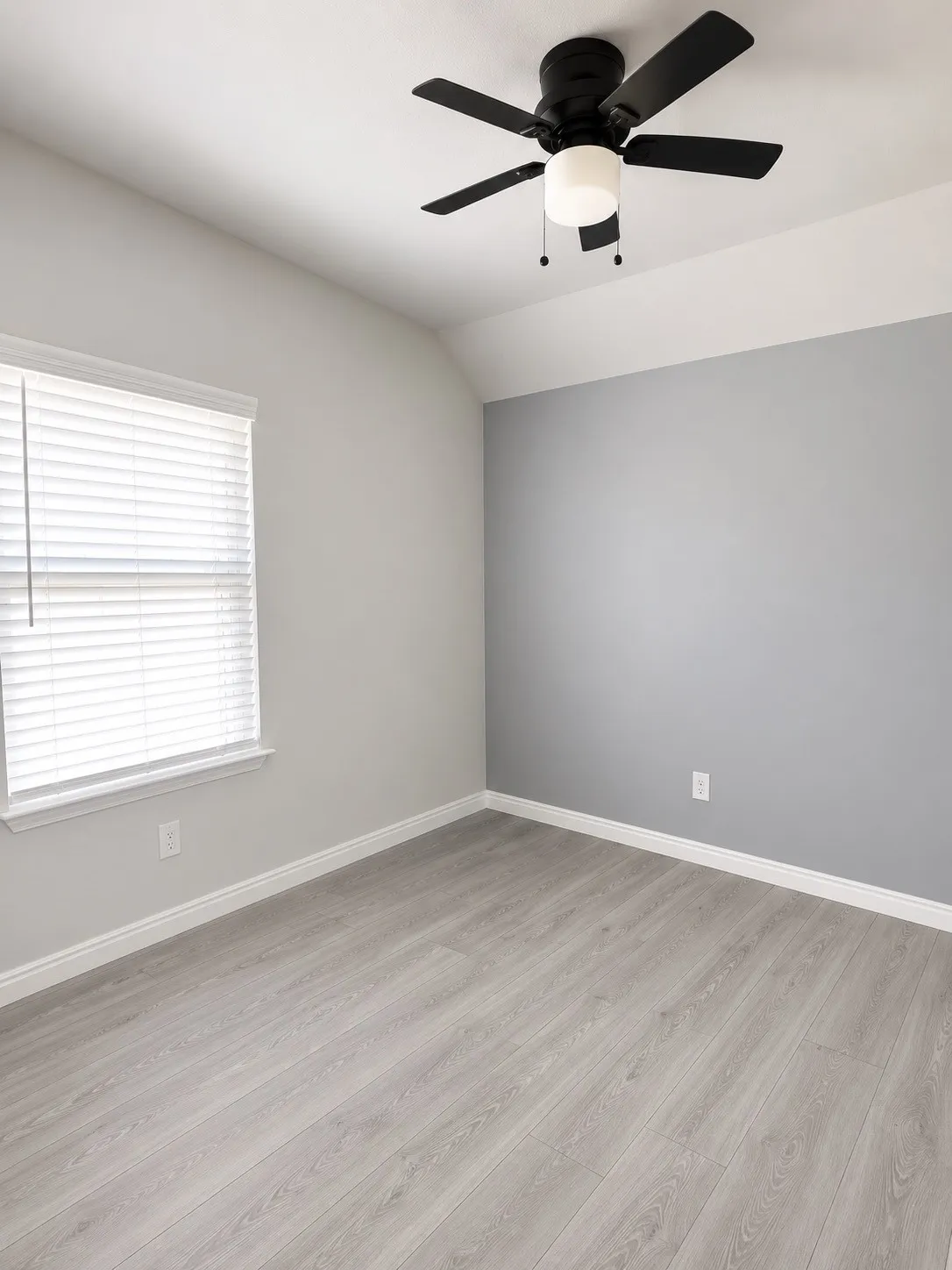 Light wood-finish flooring with a neutral color palette, ceiling fan with integrated lighting, and window with horizontal blinds