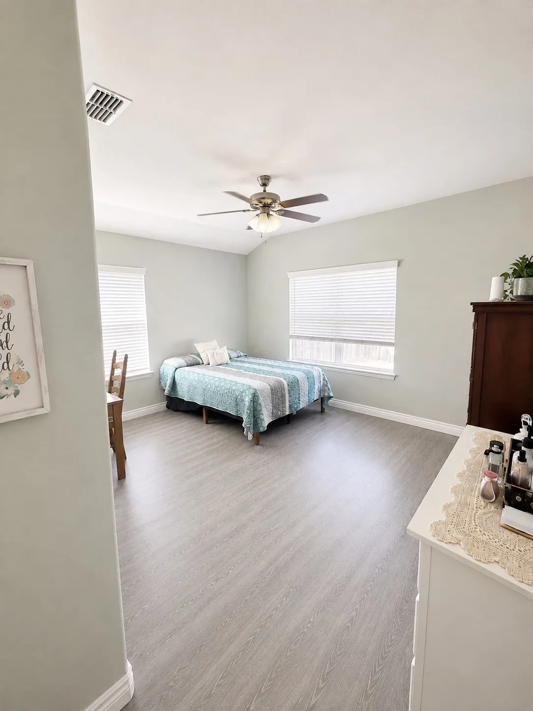 Vaulted ceiling with a ceiling fan light fixture, wood-finish flooring, and multiple windows with blinds