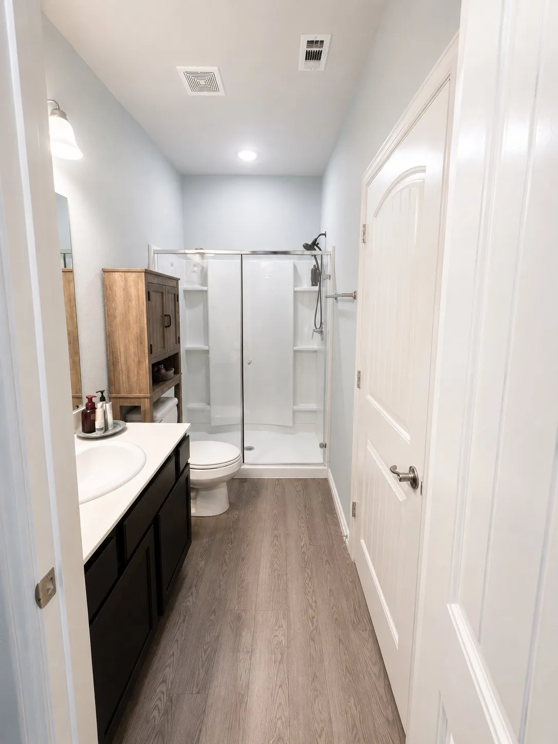 Bathroom featuring a single-sink vanity with dark cabinetry, wood-finish flooring, and a glass-enclosed shower