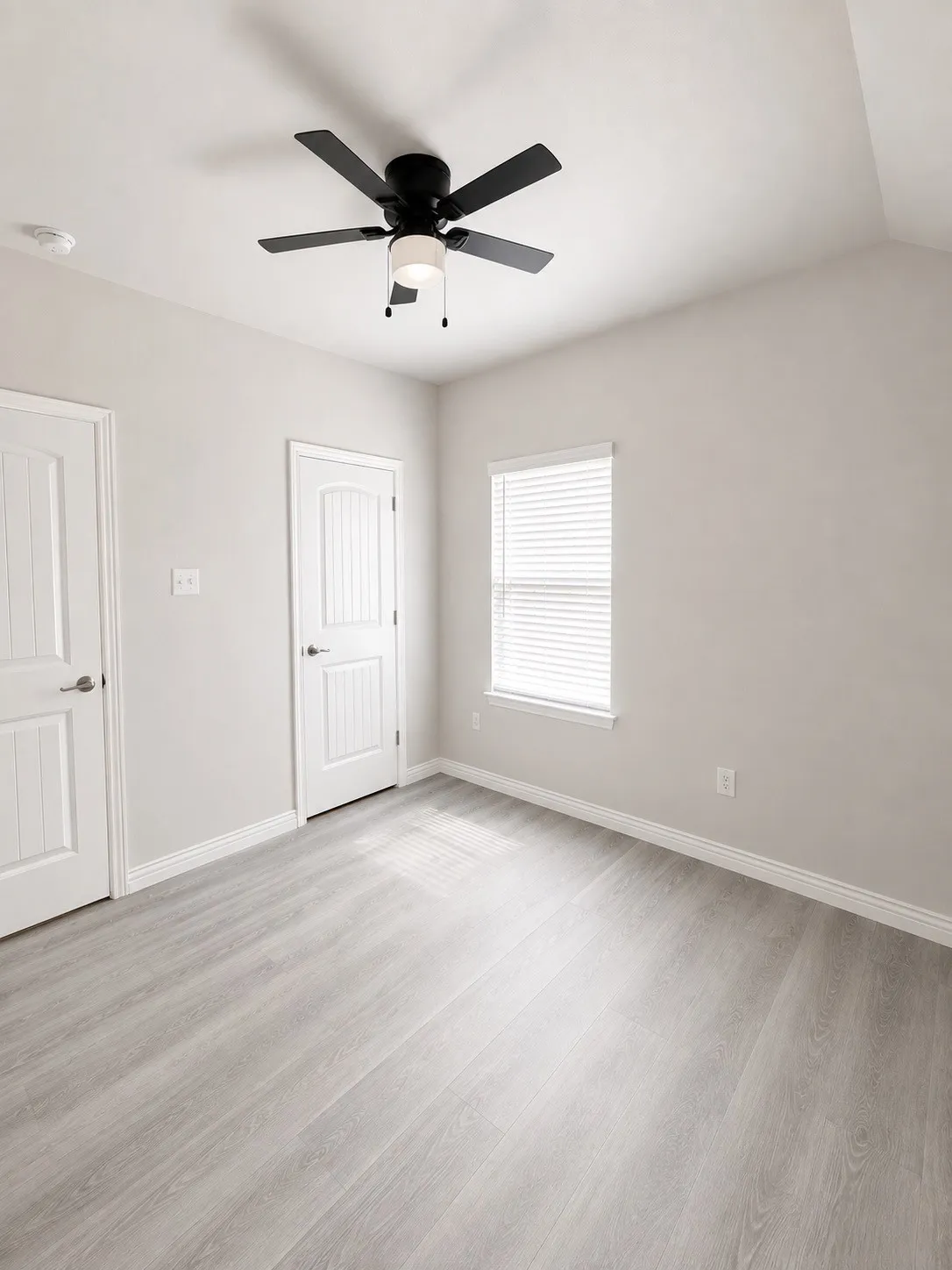 Vaulted ceiling featuring a ceiling fan with integrated lighting, two panel doors, a window with blinds, and wood-finish flooring