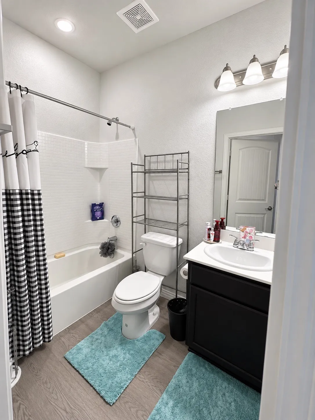 Full bathroom featuring a tub-shower combination with subway tile surround, a single vanity with a dark cabinet base, a white countertop, and wood-finish flooring