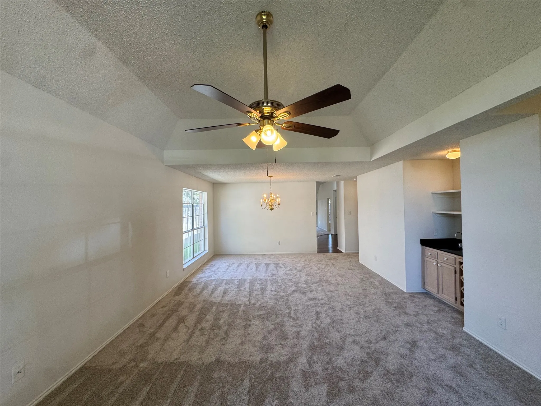 Vaulted ceiling with a ceiling fan, broad window, and built-in wet bar with shelving
