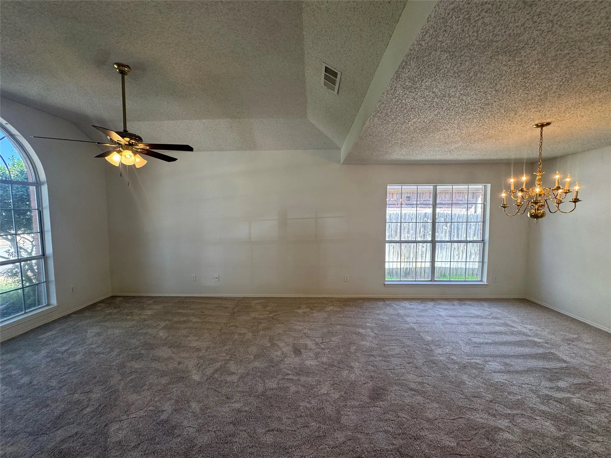Vaulted ceiling, arched window, ceiling fan with integrated lighting, chandelier, and wall-to-wall carpeting