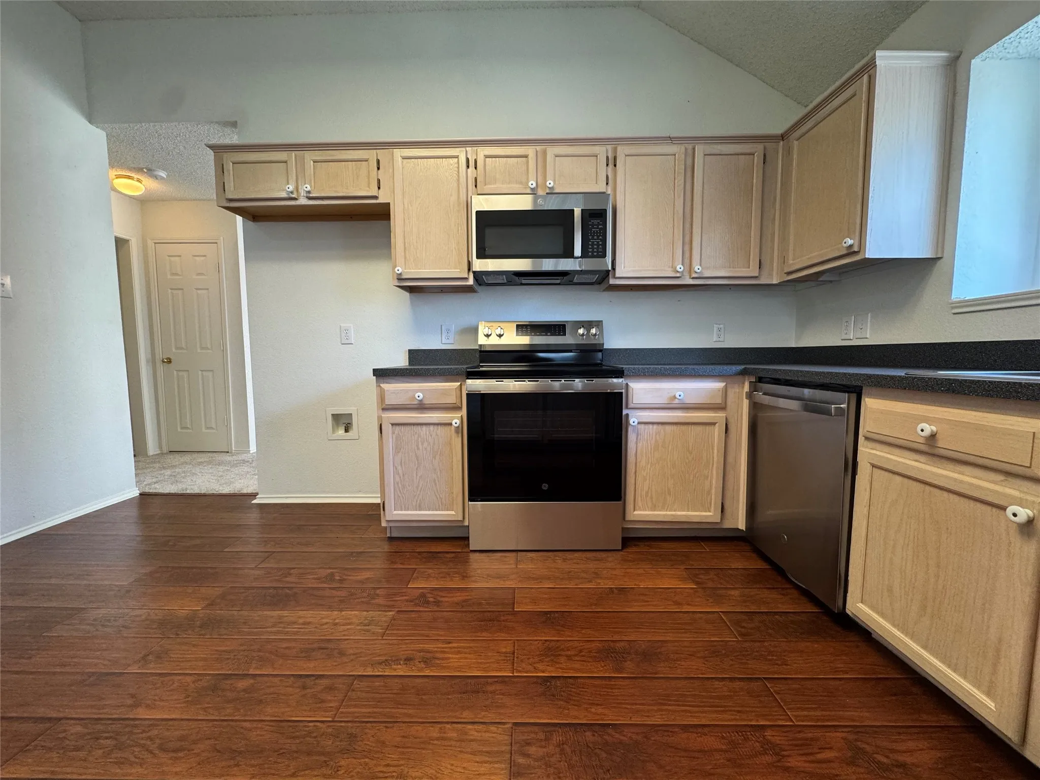 Kitchen featuring wood-finish flooring, light wood cabinetry, dark countertops, and stainless steel appliances