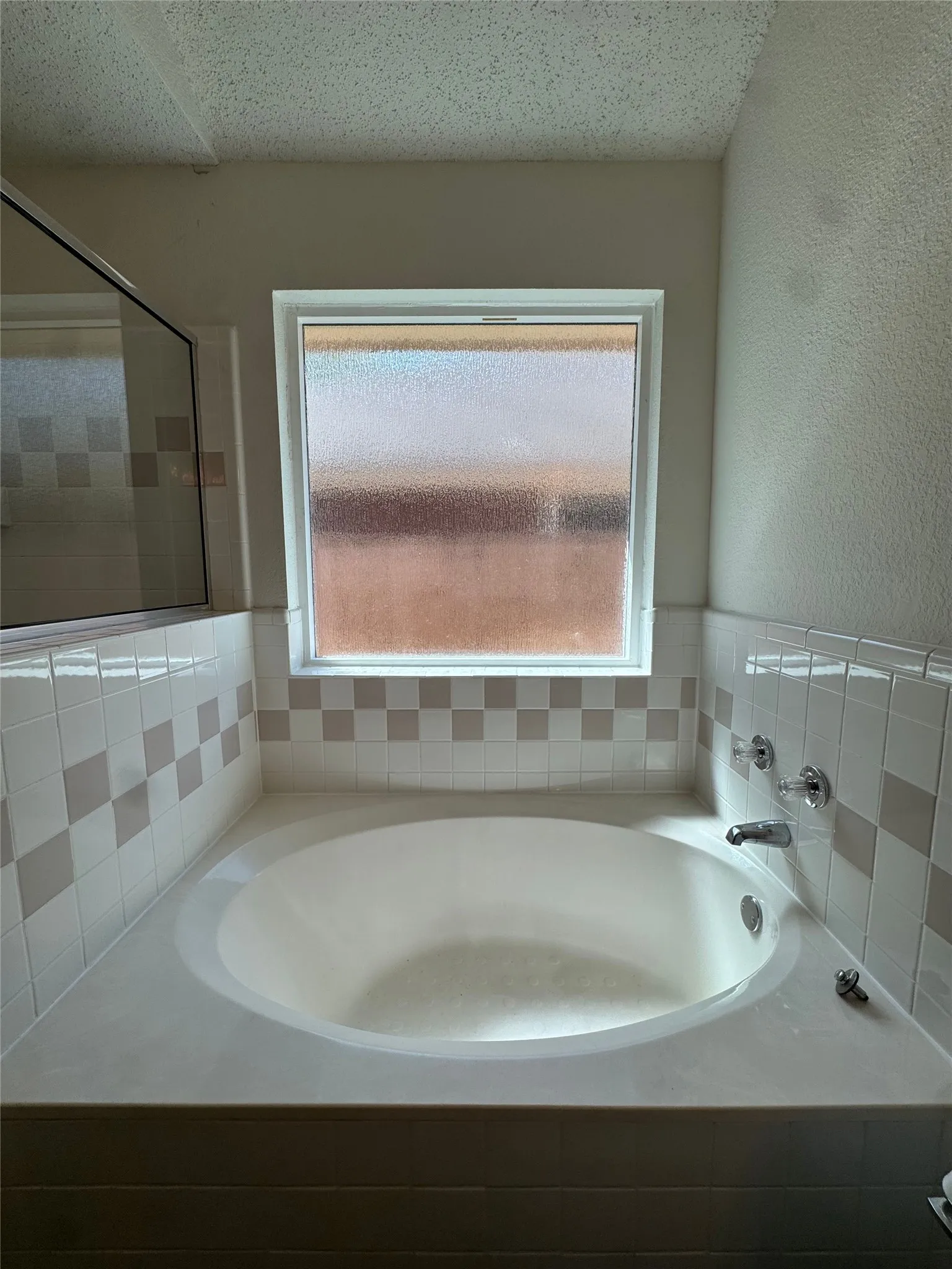 Built-in soaking tub with deck-mounted fixtures, accented by patterned wall tile and a privacy window
