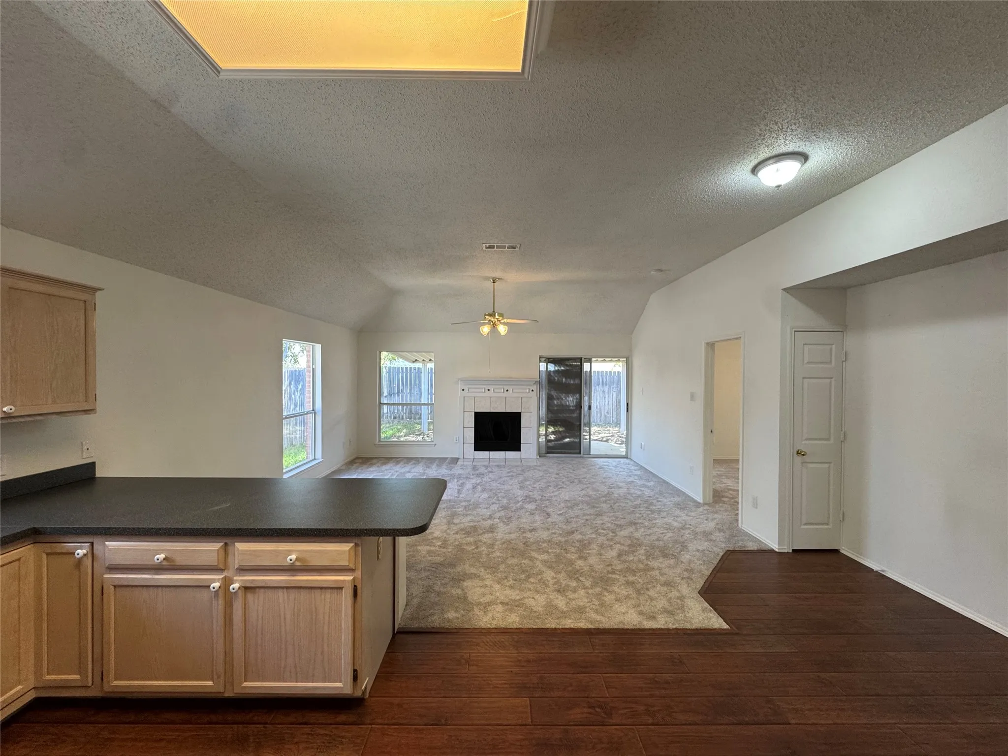Vaulted ceilings with a skylight, wood-finish flooring, built-in fireplace, sliding glass door, and a kitchen peninsula with cabinetry