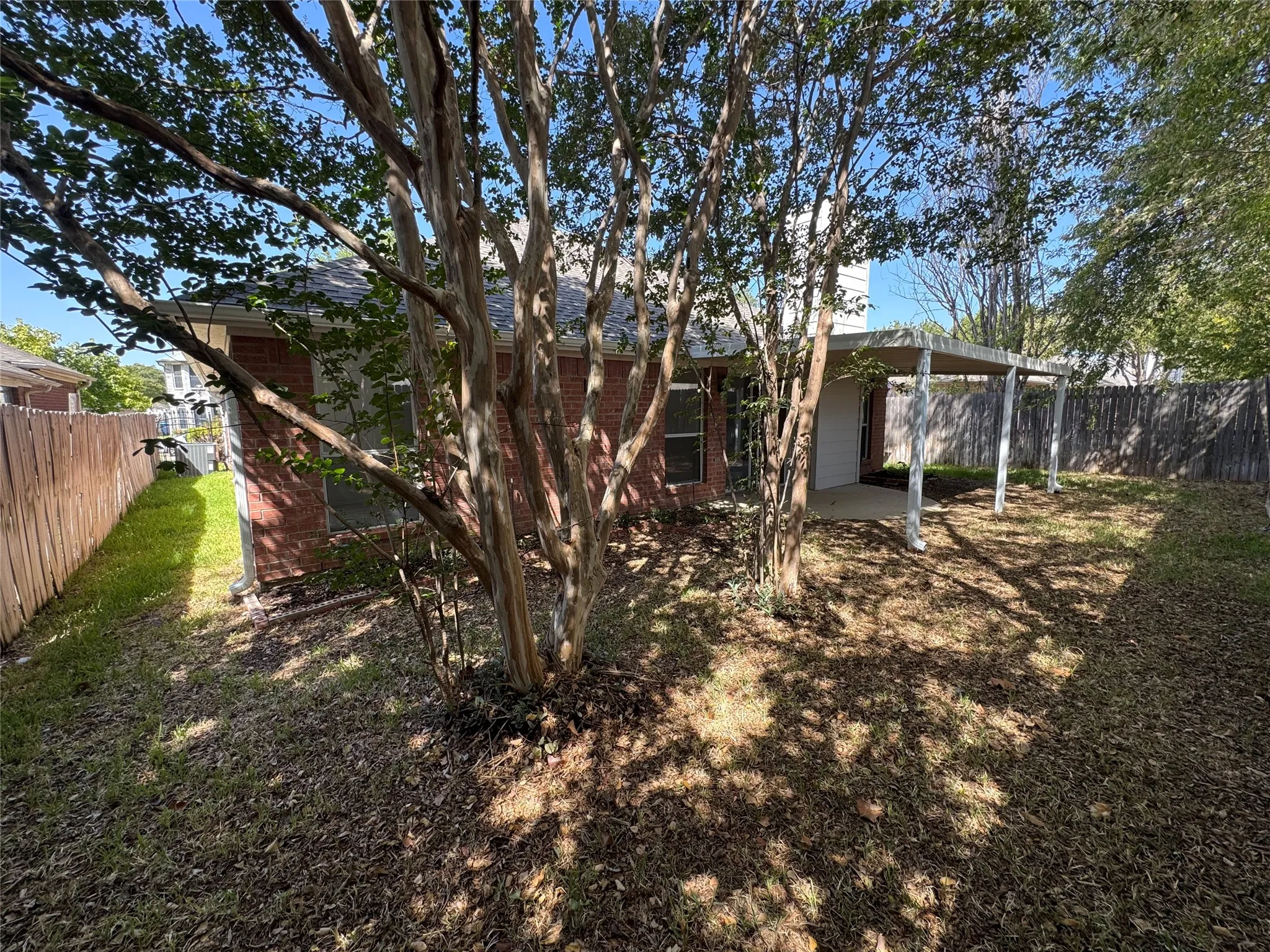 Rear yard featuring a covered patio, mature trees, and a wood privacy fence