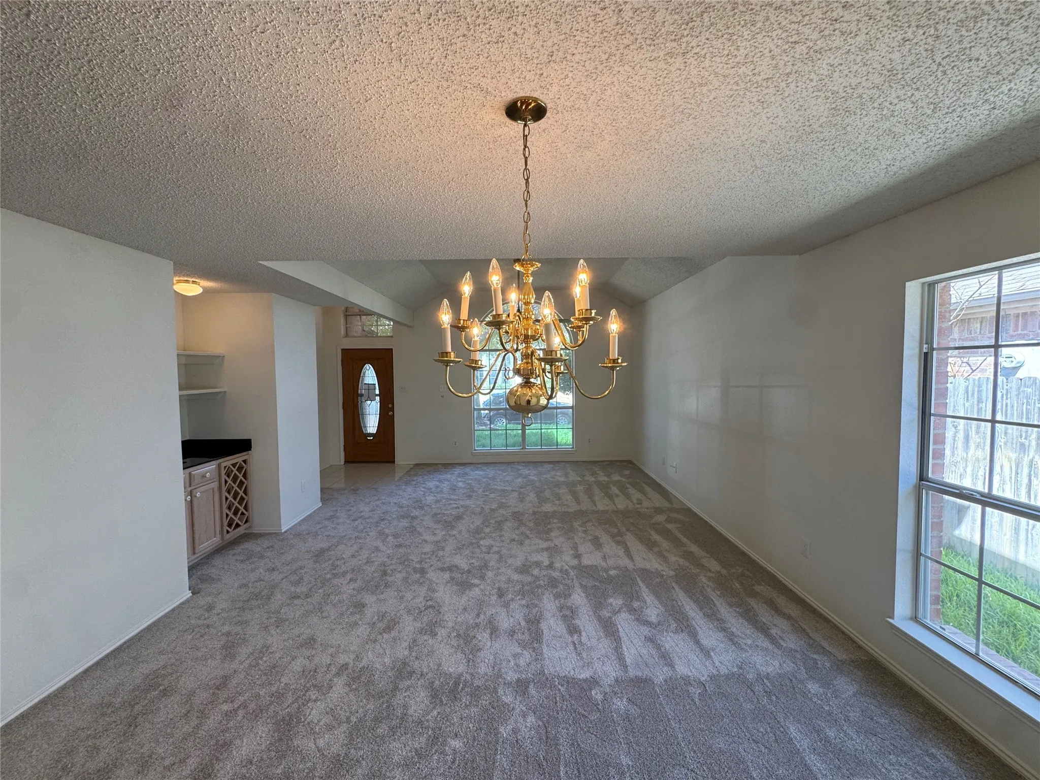 Carpeted living area with a brass chandelier, large window, and built-in cabinetry with a countertop