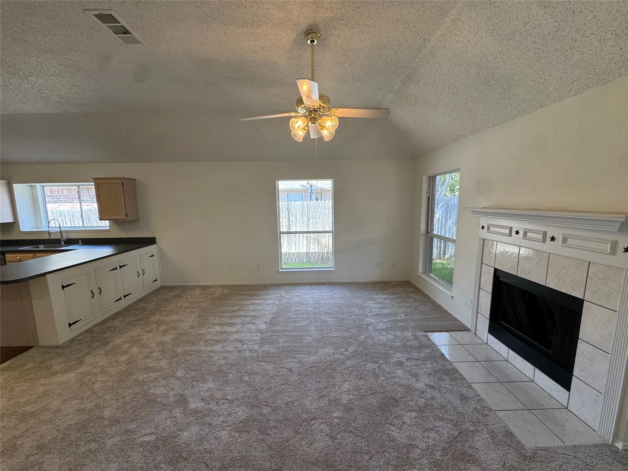 Vaulted ceiling, ceiling fan with integrated lighting, tiled fireplace with mantel, built-in cabinetry, and multiple windows