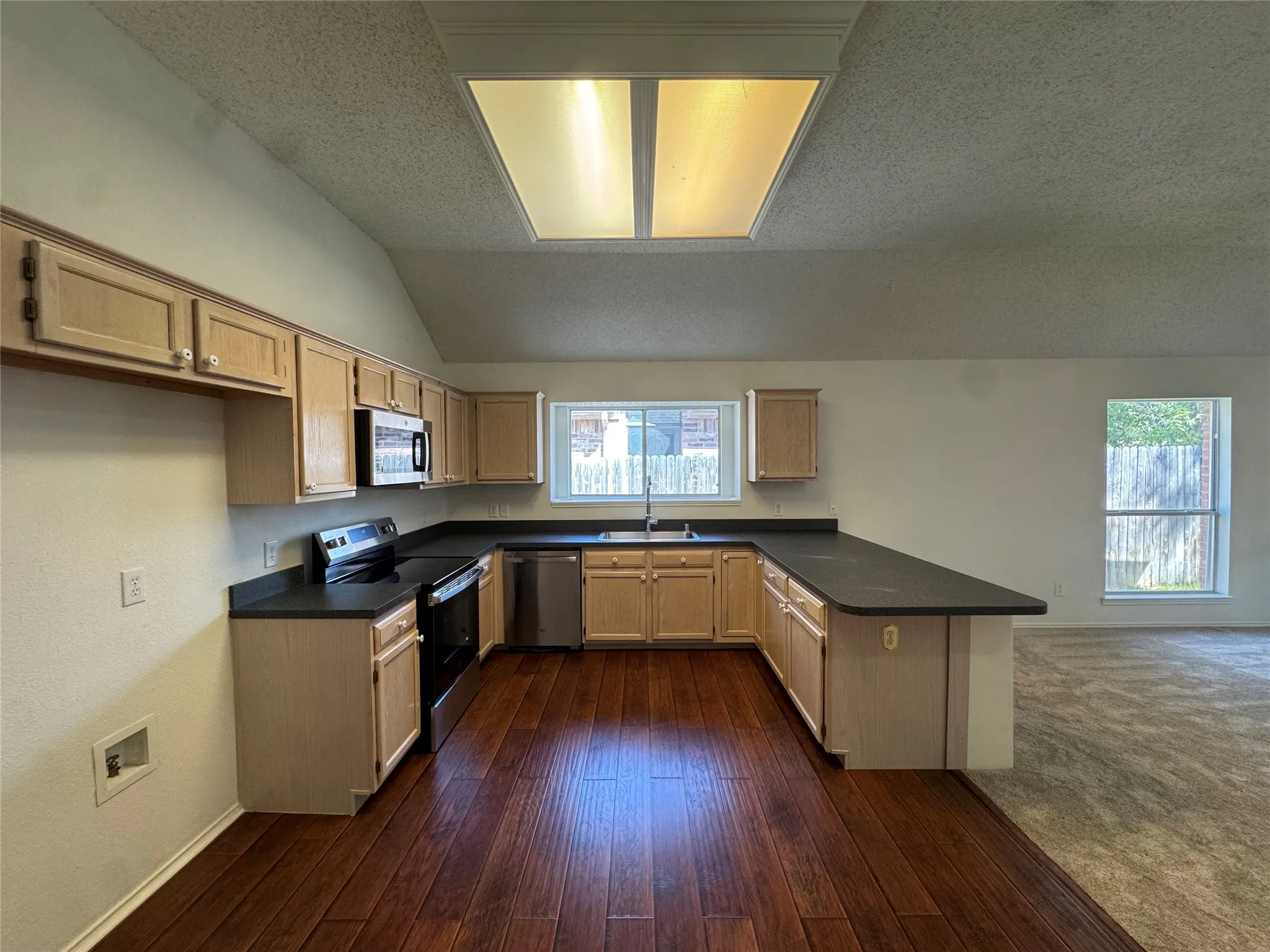 Kitchen featuring wood-finish flooring, light wood cabinetry, dark countertops, and a skylight