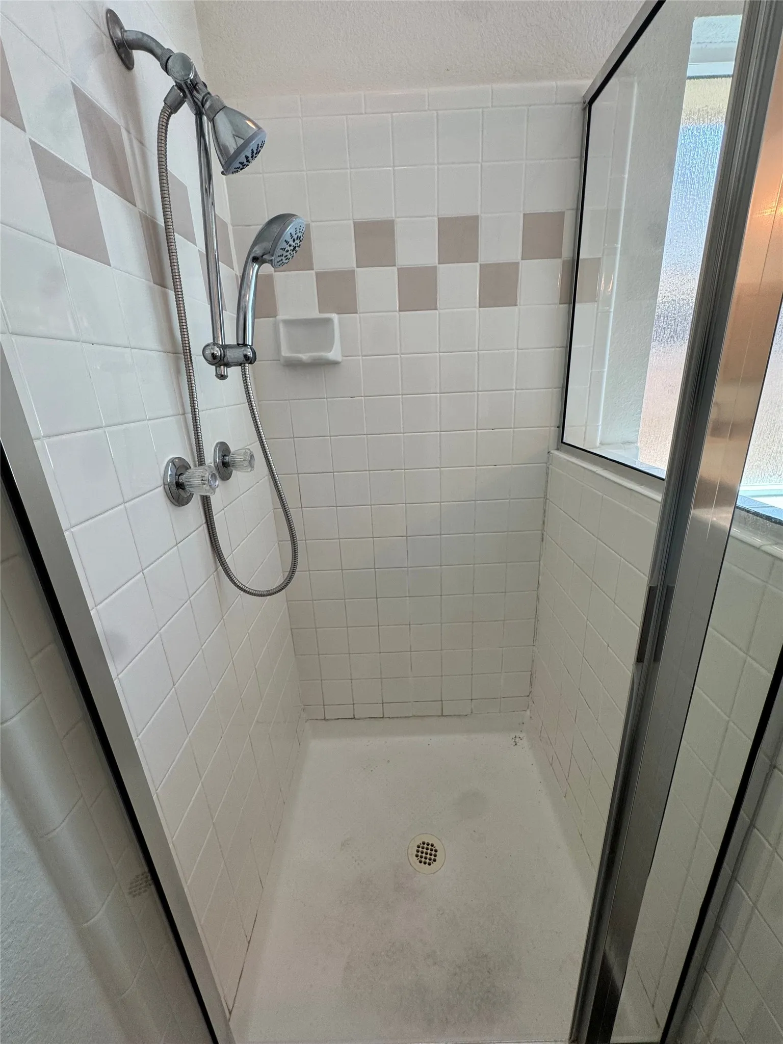 Tiled shower enclosure featuring a dual shower head system and a clear glass shower door