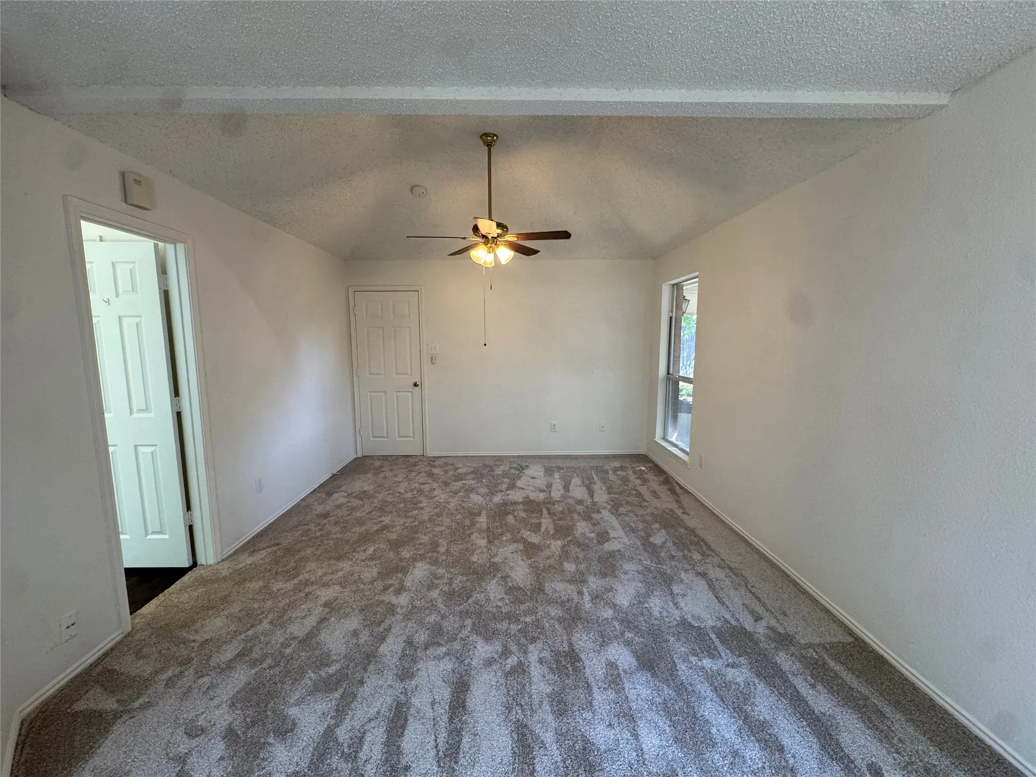 Vaulted ceiling with exposed beam, ceiling fan, carpet flooring, and a single window