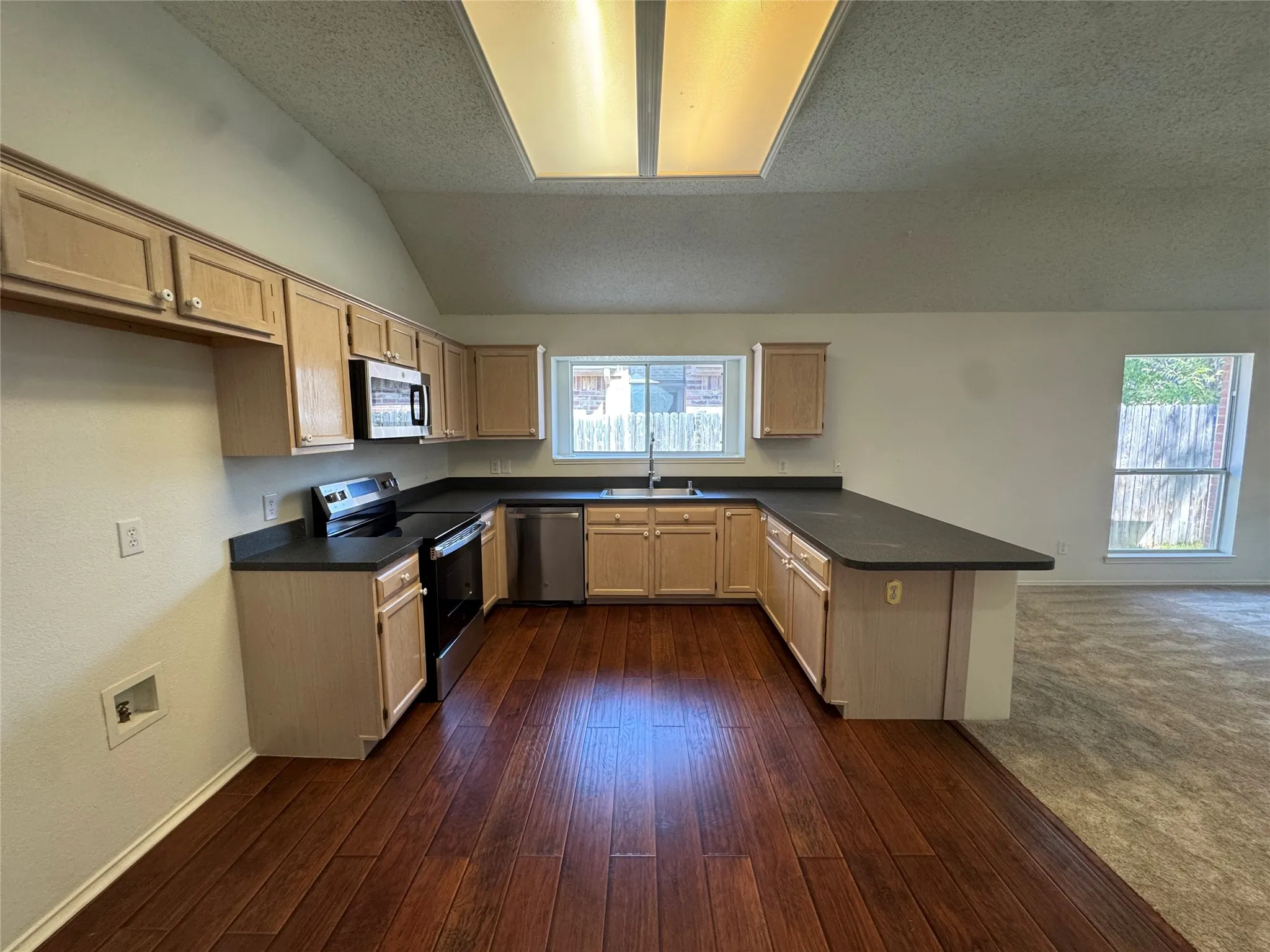 Kitchen featuring wood-finish flooring, light wood cabinetry, stainless steel appliances, dark countertops, and a window over the sink