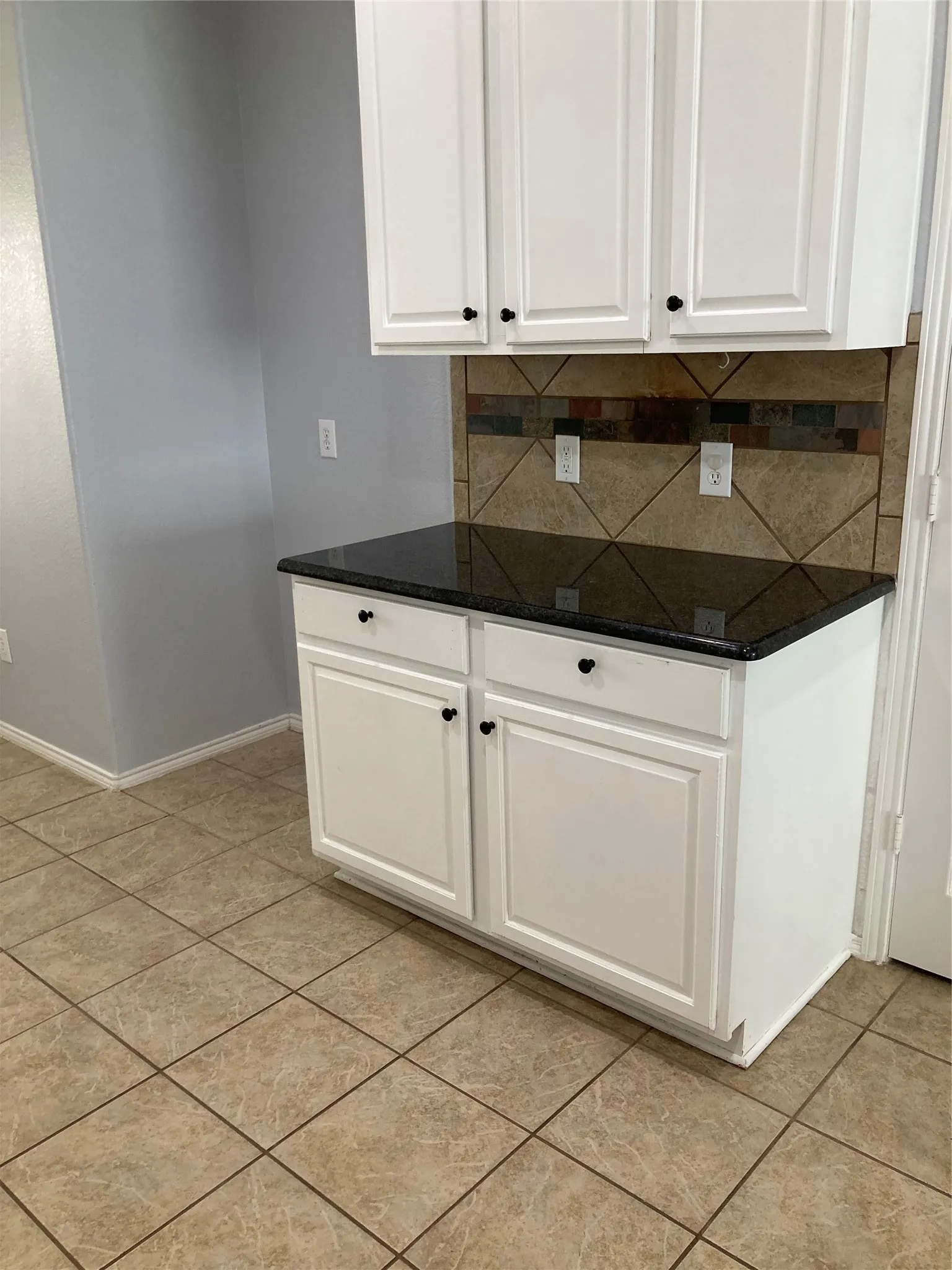Extra cabinets in the kitchen are located on a wall next to the refrigerator space.