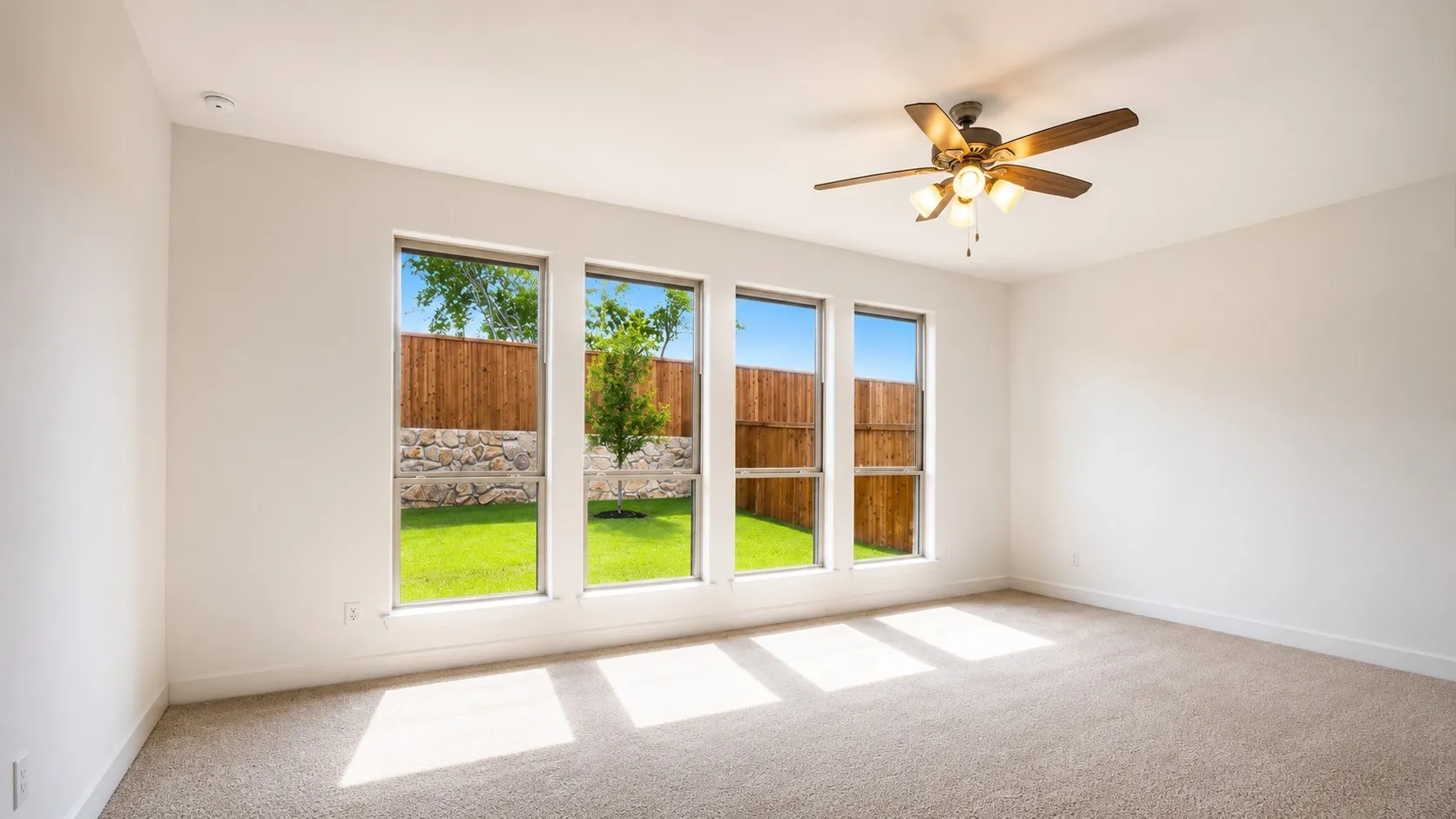 Light-filled room featuring a ceiling fan with integrated lighting, four tall windows, and neutral carpeting