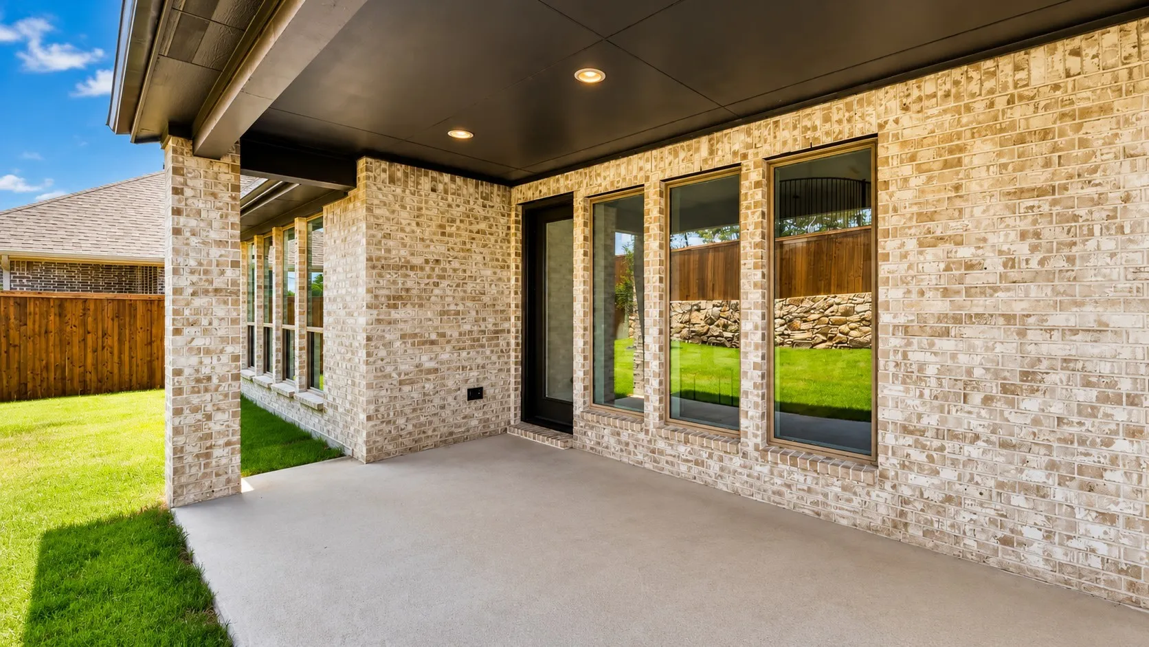 Covered patio with recessed lighting, light-toned brick exterior, and a manicured lawn
