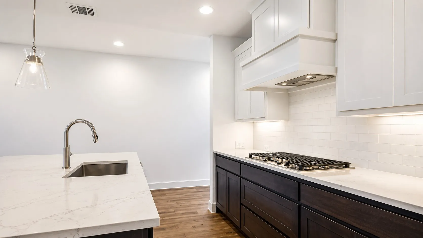 Quartz countertops, stainless steel sink with pull-down faucet, gas range, white shaker-style upper cabinetry, and wood-finish flooring