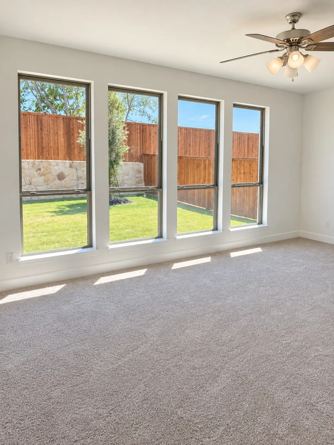 Carpeted room with four large vertical windows, a built-in ceiling fan with integrated lighting, and painted walls