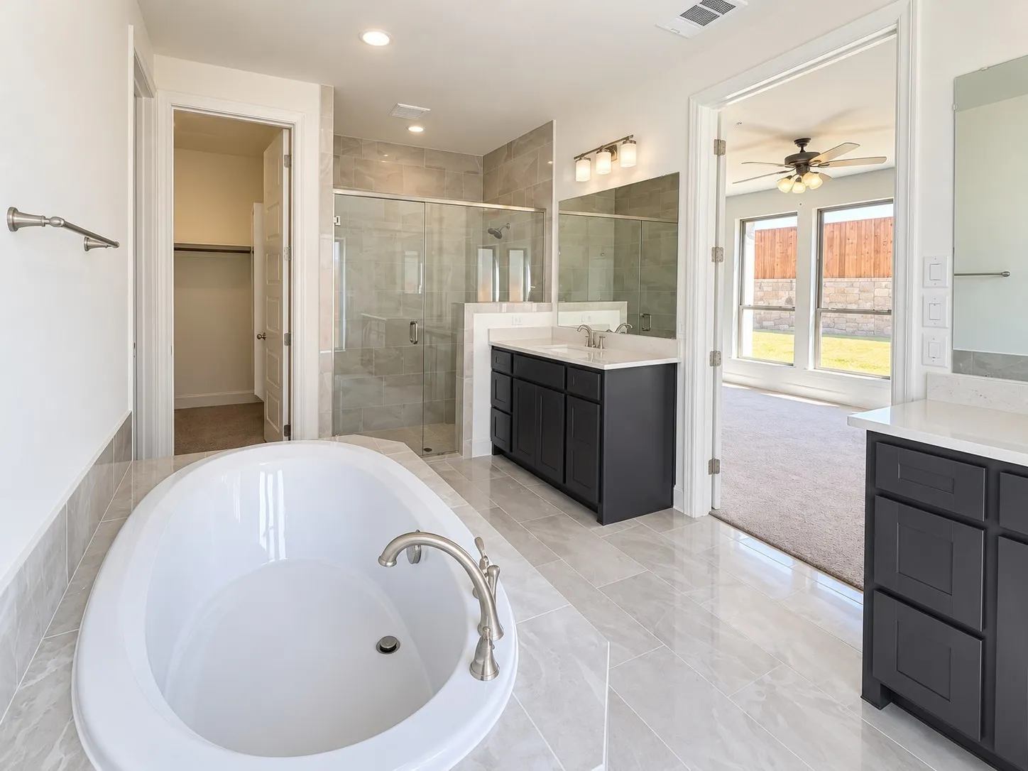 Soaking tub with brushed nickel fixtures, dual vanities with white countertops, glass-enclosed shower, and tile flooring