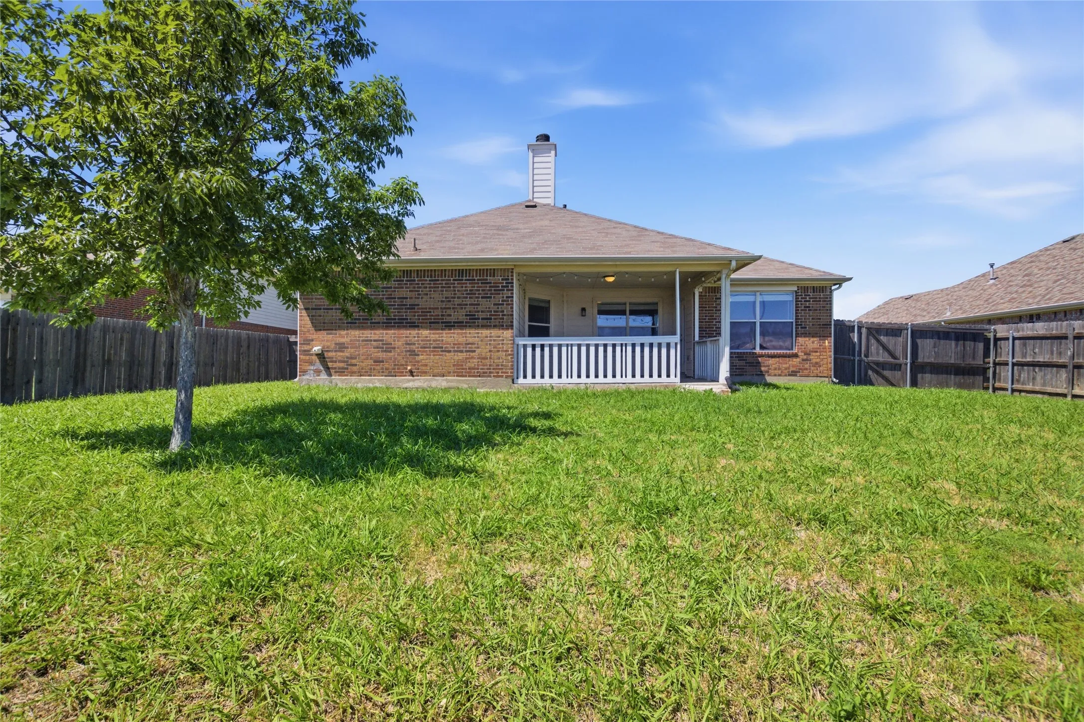 Expansive backyard featuring a brick exterior, covered patio with white railing, and wood fencing