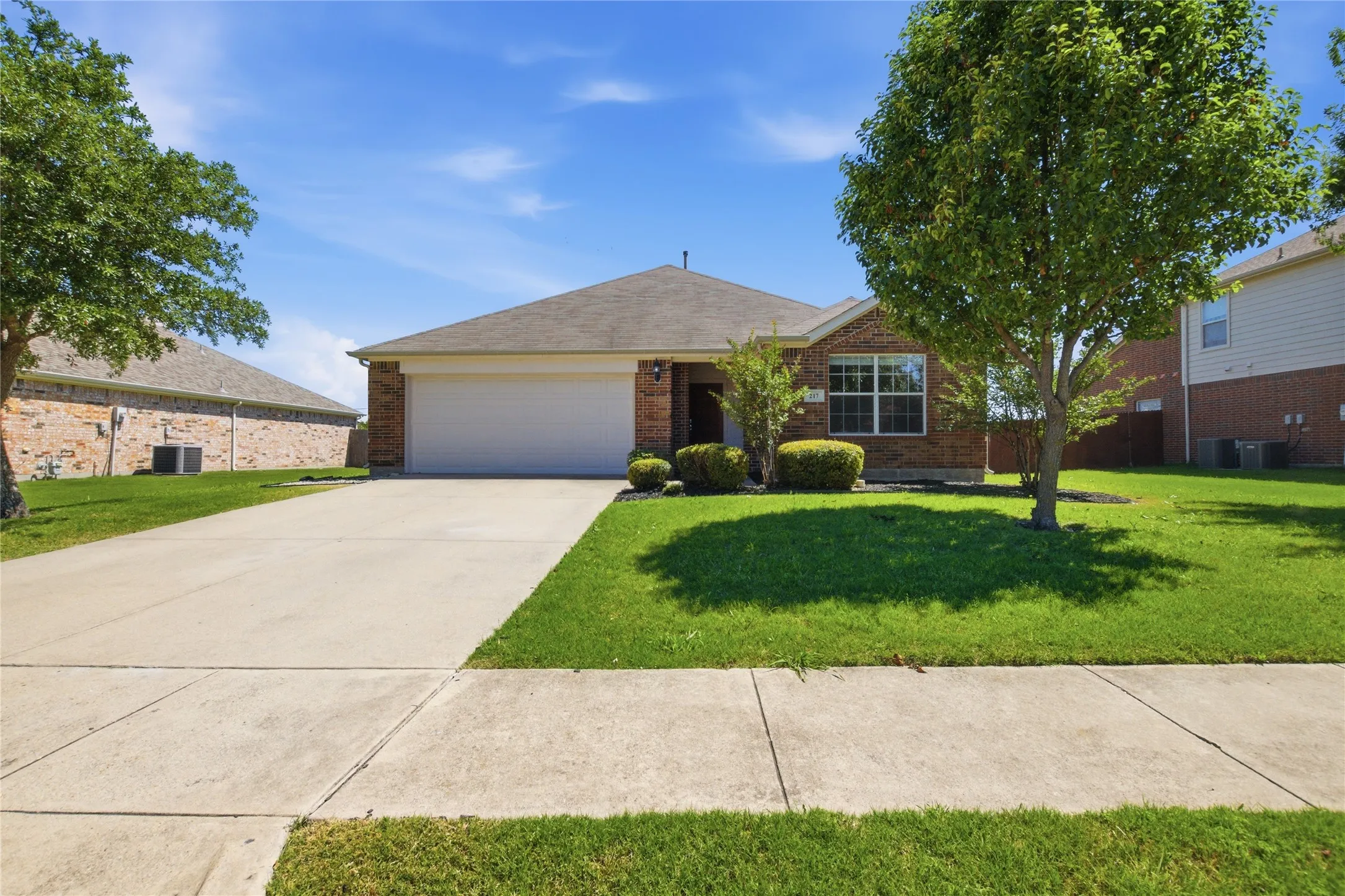 Brick facade, attached garage, concrete driveway, mature trees, manicured lawn