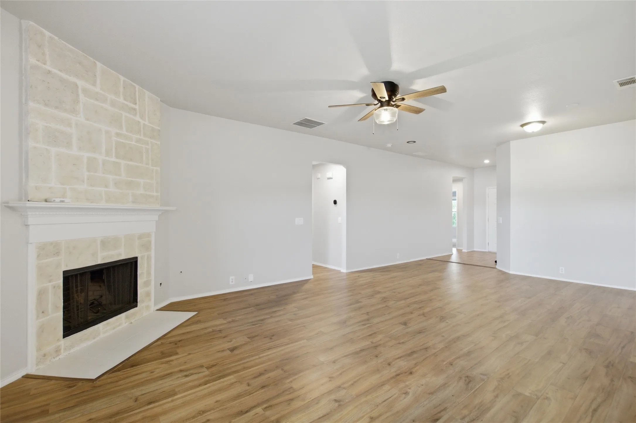Spacious room featuring a stone-clad fireplace with a classic mantel, wood-finish flooring, and a ceiling fan with integrated lighting