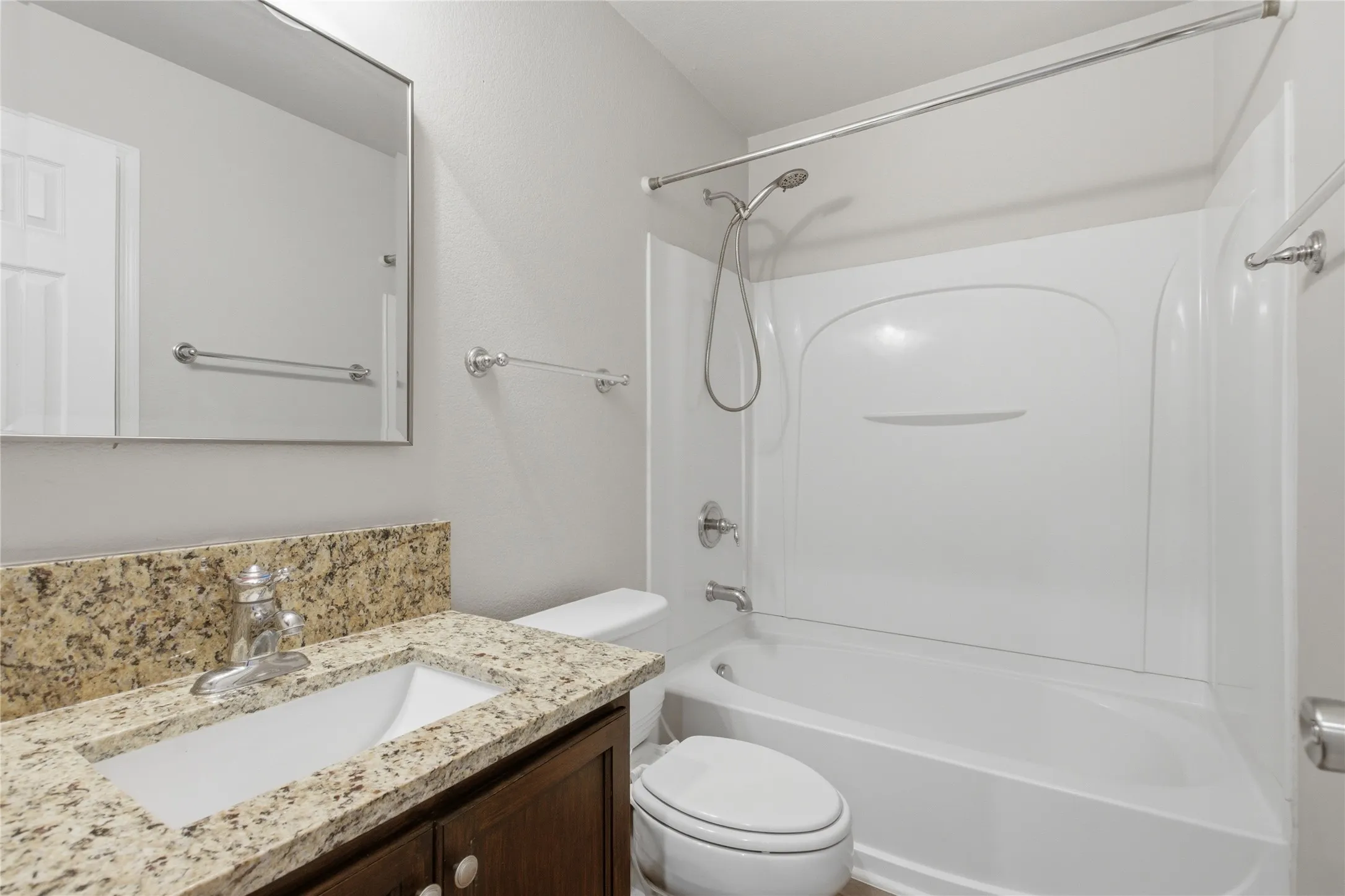 Bathroom featuring a vanity with a granite-look countertop, integrated sink, chrome faucet, and a shower-tub combination with a white surround