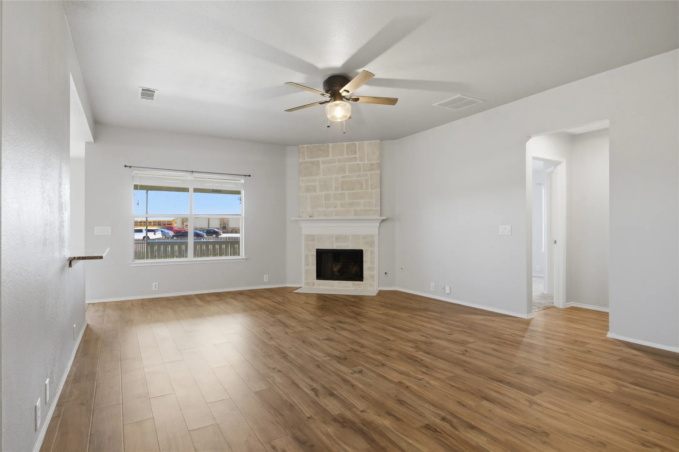 Expansive living area featuring wood-finish flooring, a stone-clad fireplace with a mantel, a ceiling fan, and a large window