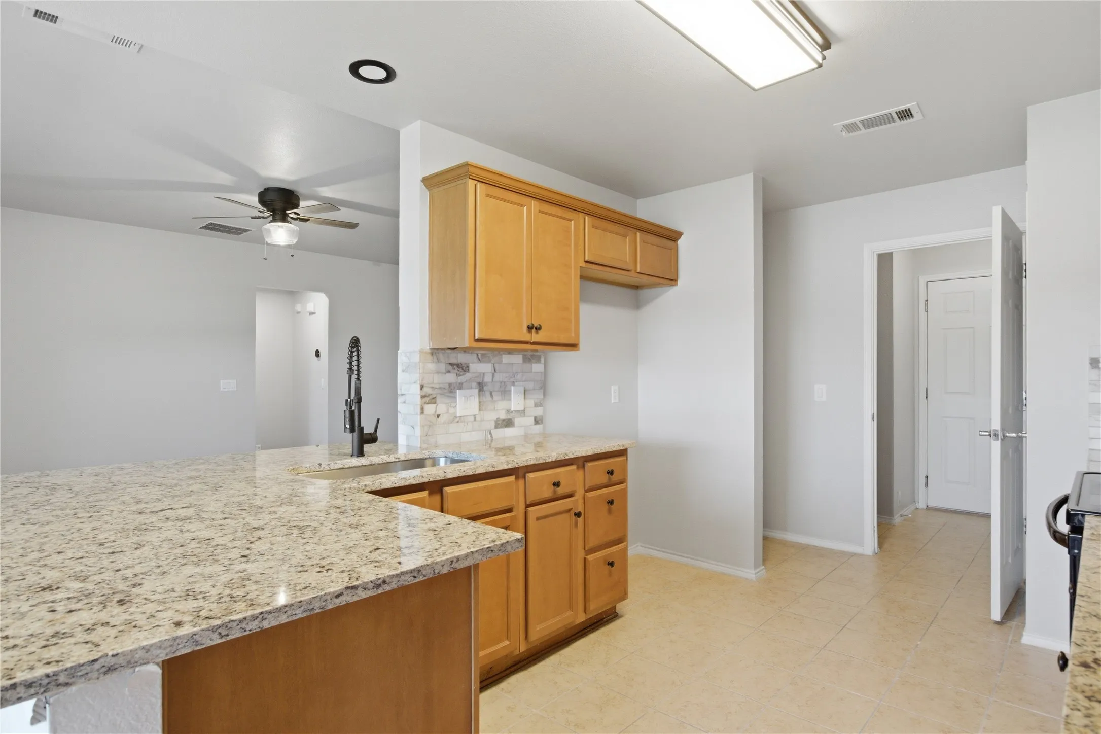 Kitchen featuring light wood cabinetry, stone countertops, a stainless steel sink with a matte black faucet, and a tiled backsplash