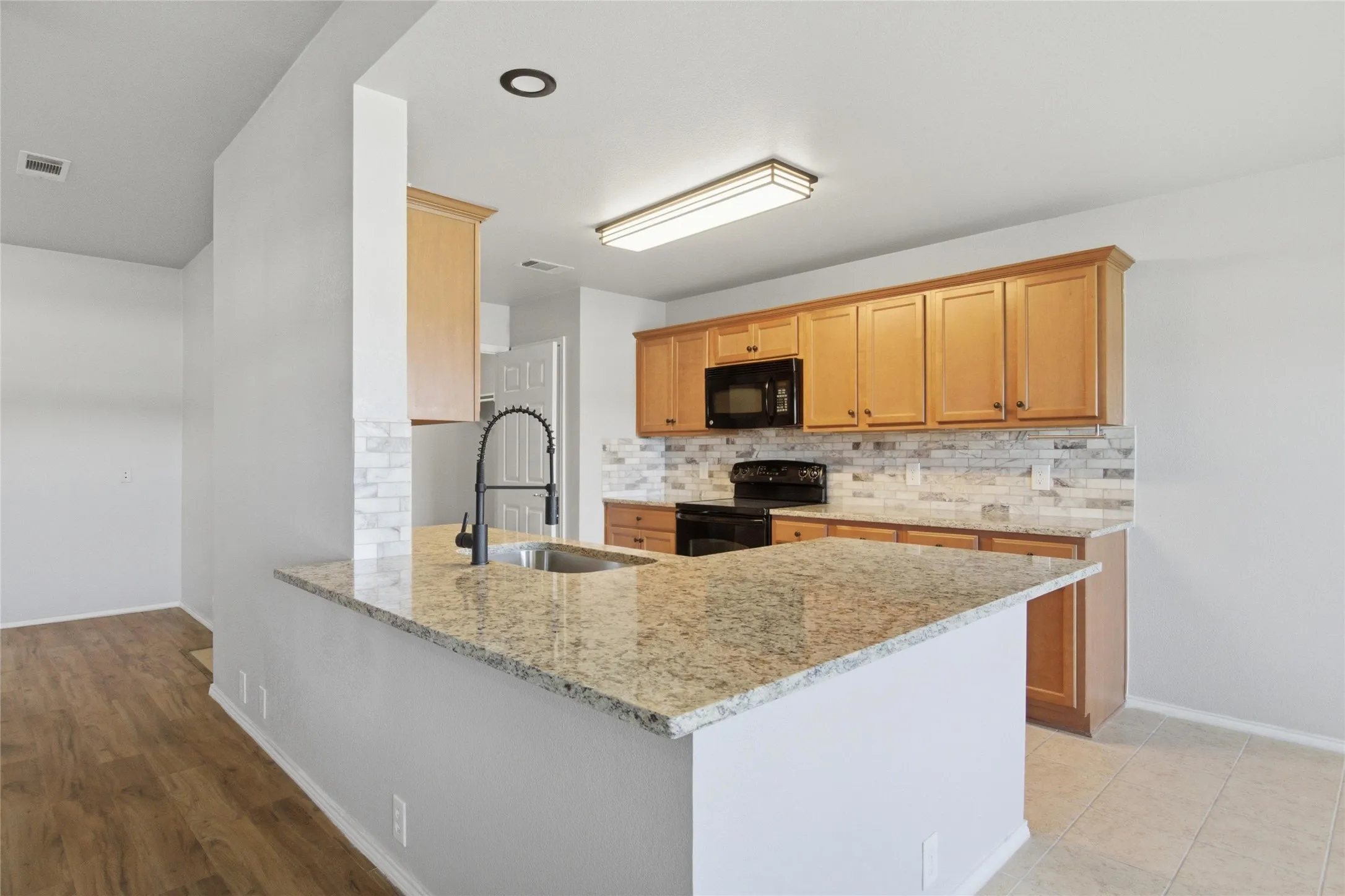 Kitchen featuring granite countertops, wood cabinetry, a tile backsplash, and black appliances