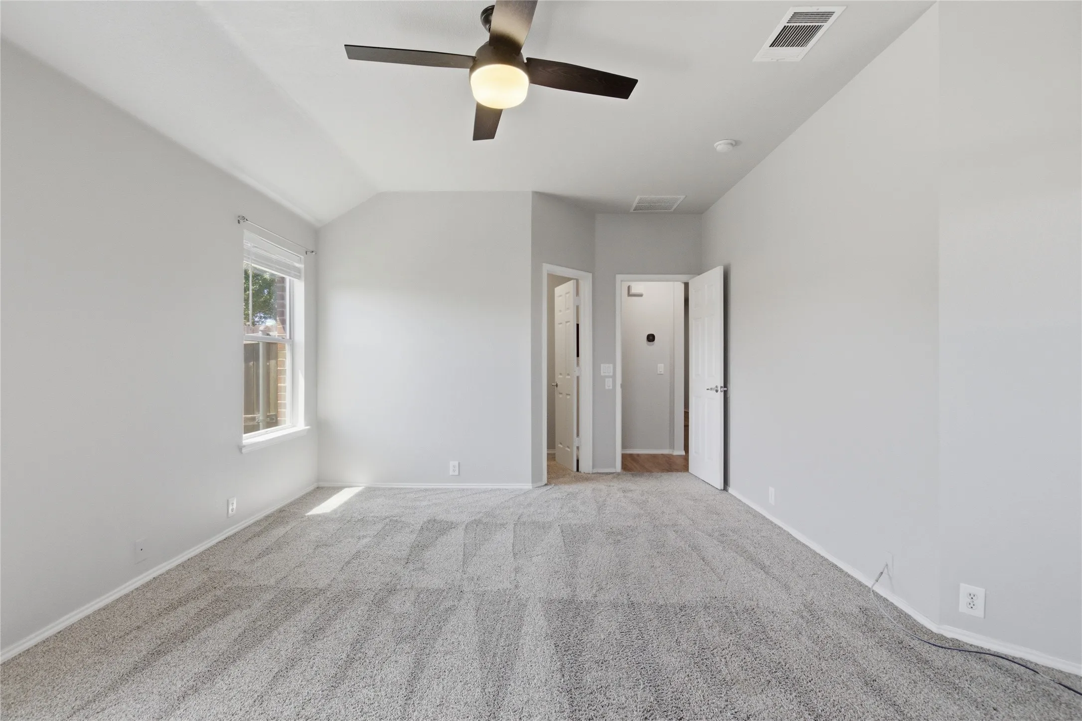 Spacious room featuring gray carpeting, a window, and a ceiling fan with integrated lighting