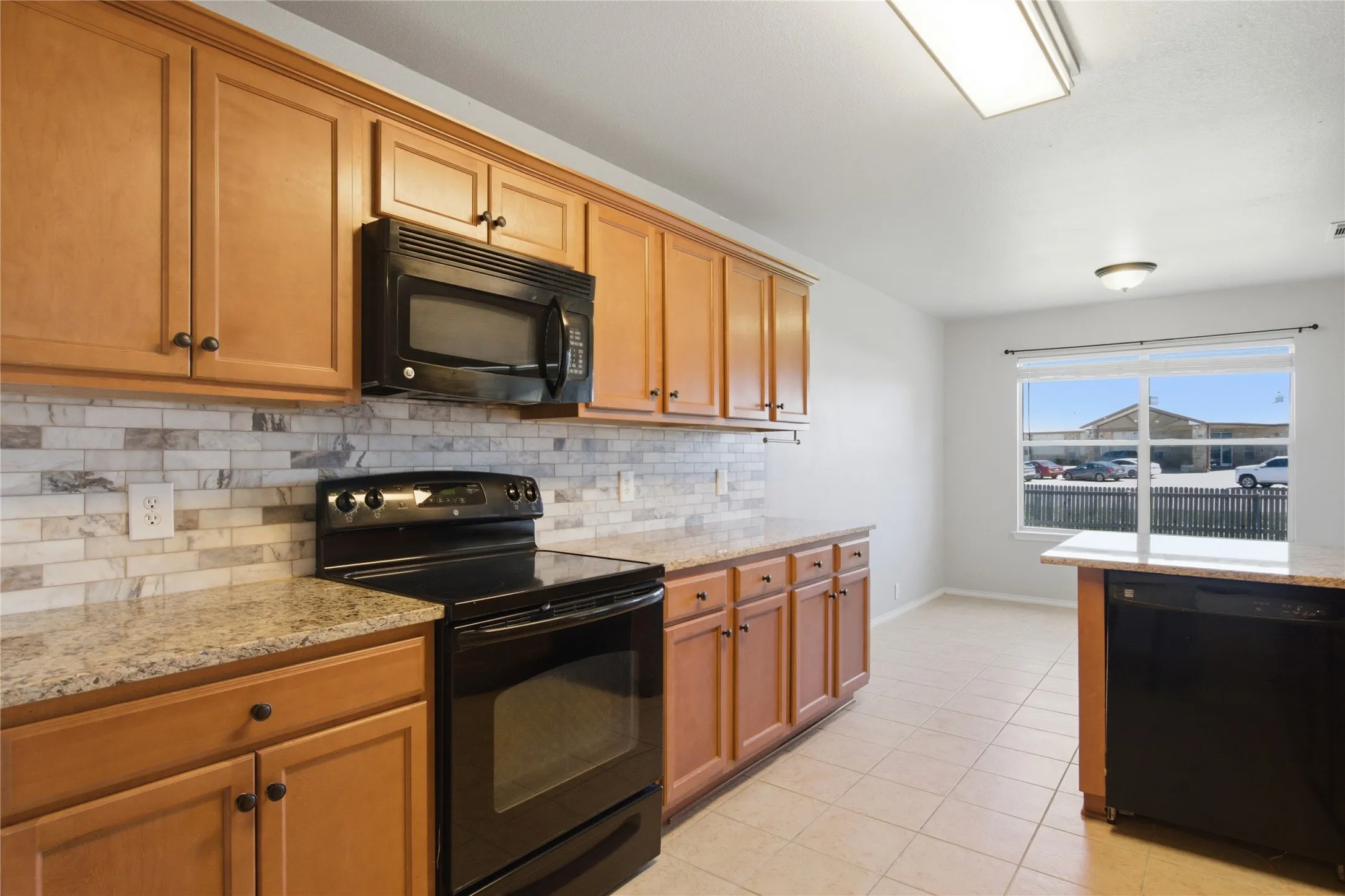 Wood-finish cabinetry, tile backsplash, stone-finish countertops, black appliances, and tile flooring