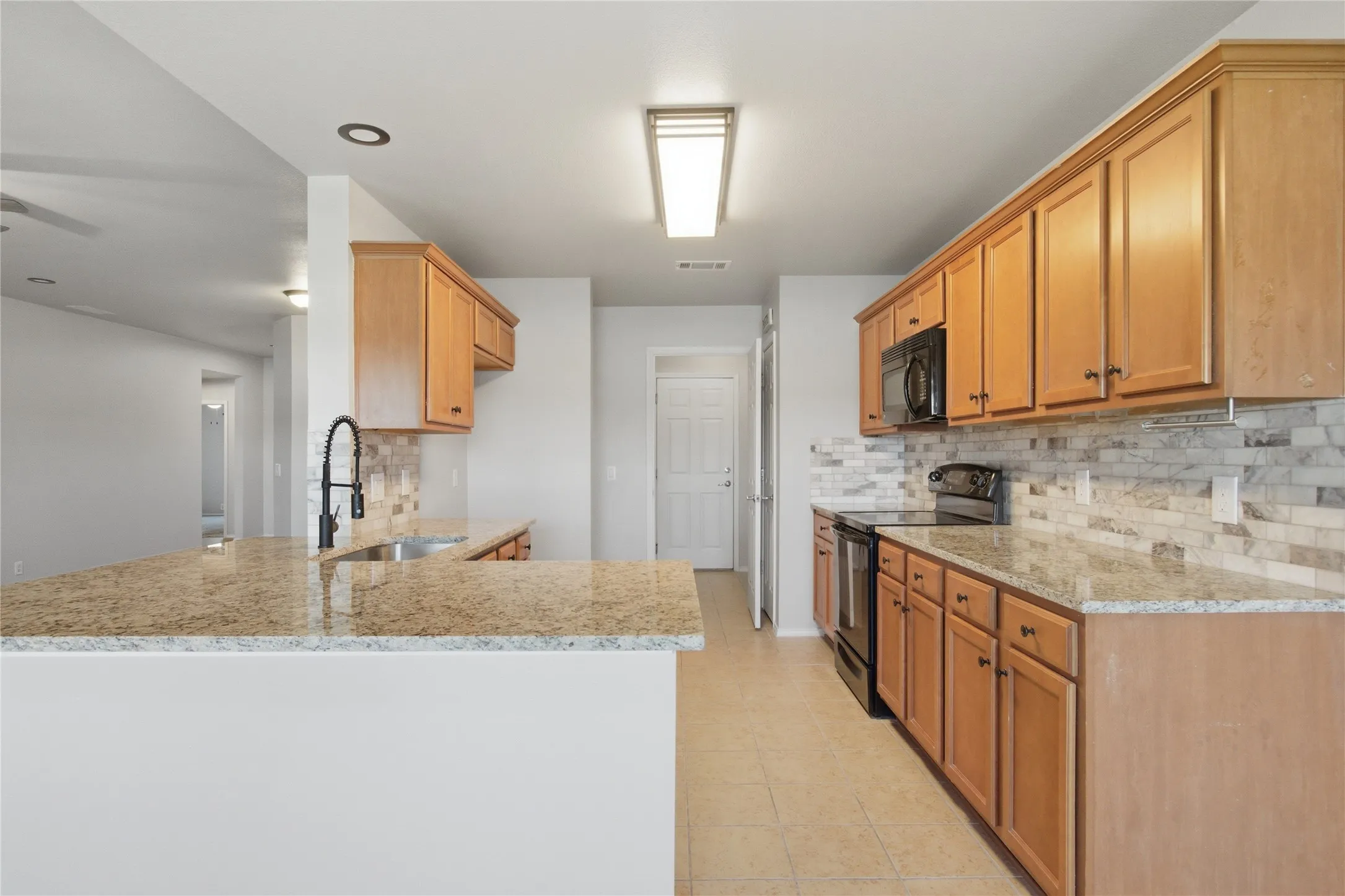 Kitchen featuring wood cabinetry, granite countertops, tile backsplash, and a black appliance suite