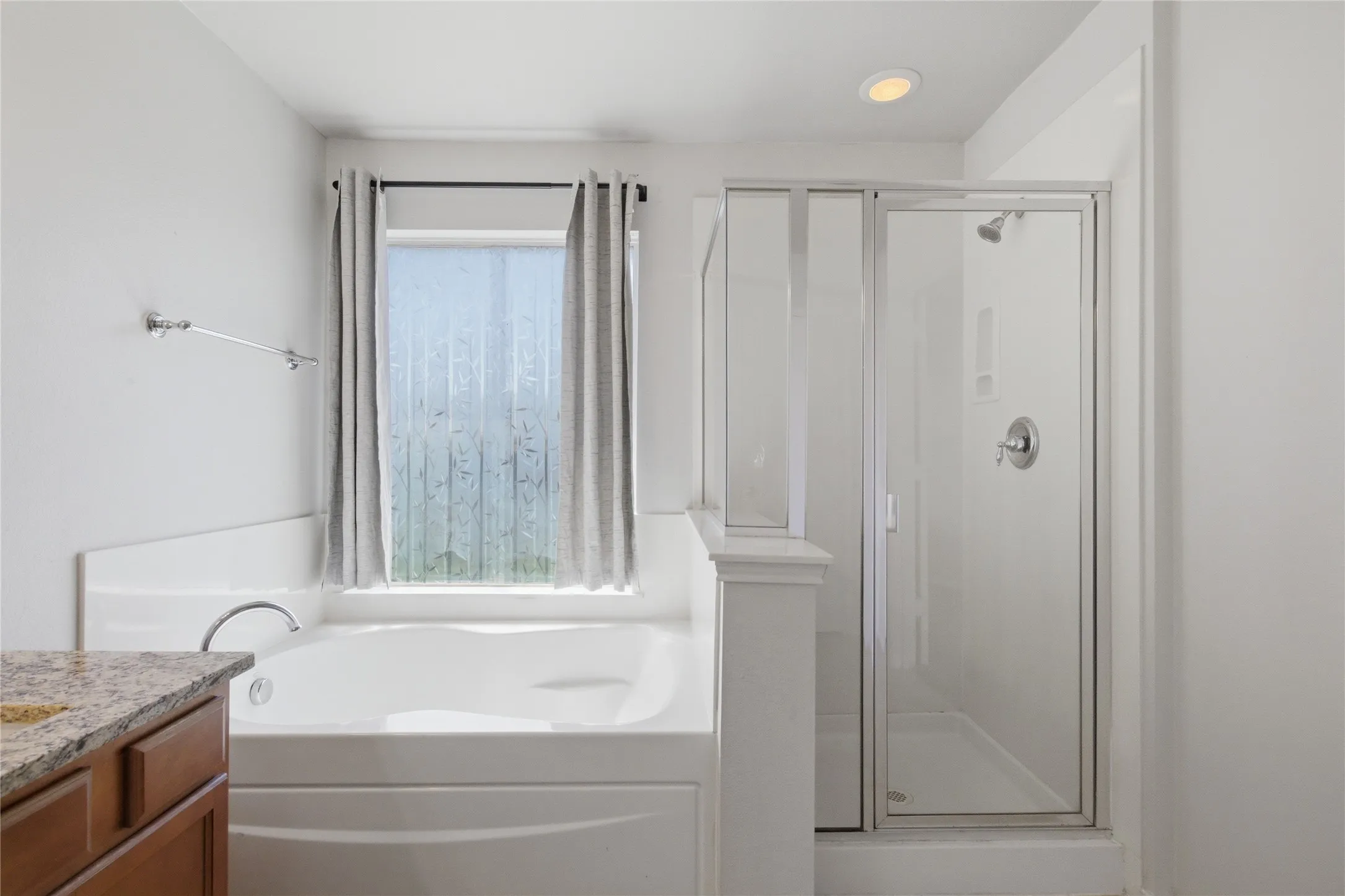 Built-in soaking tub, separate glass-enclosed shower, single vanity with wood cabinetry, and recessed lighting