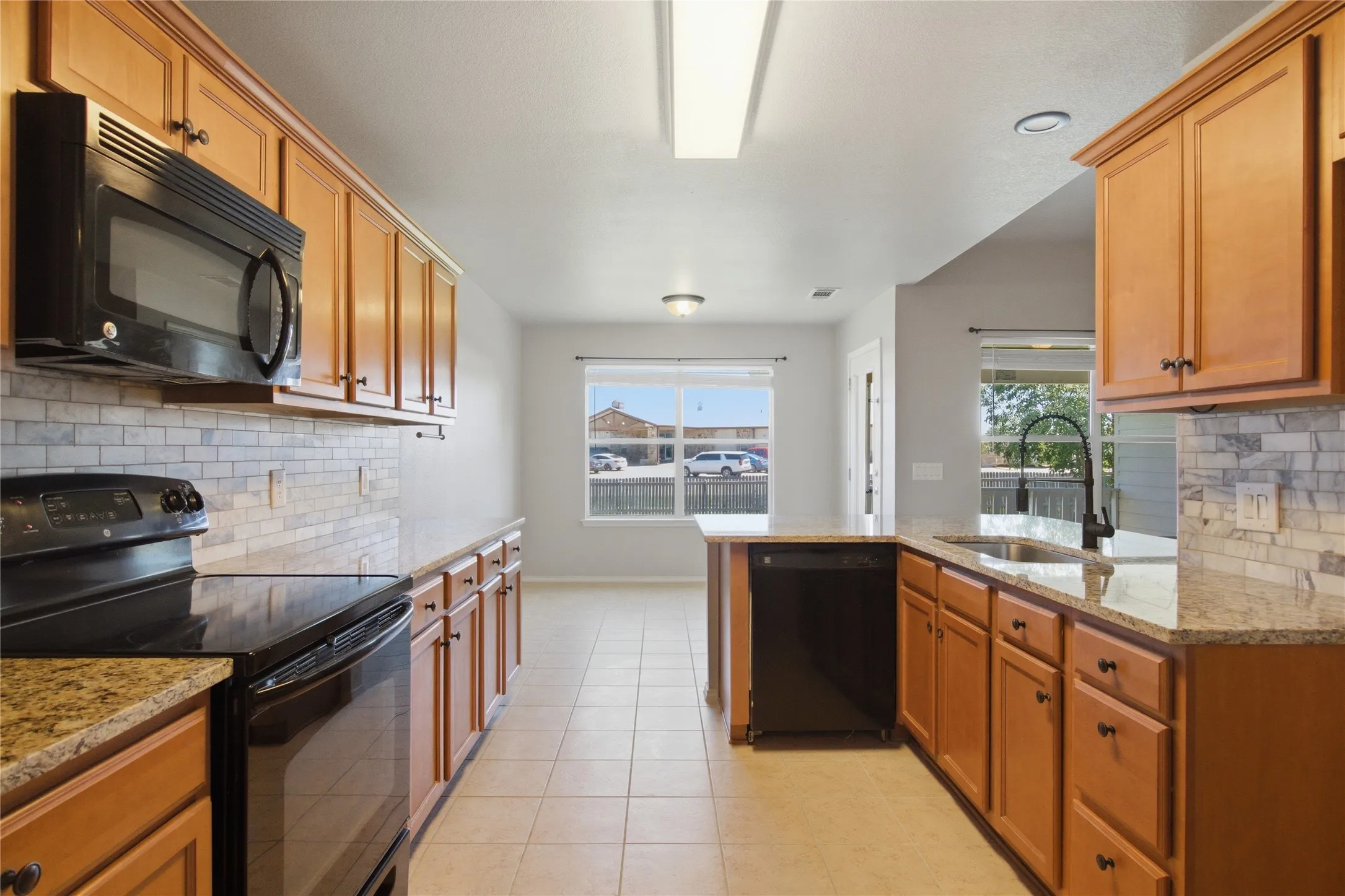Well-appointed kitchen featuring wood-finish cabinetry, black appliances, granite countertops, tile backsplash, and tile flooring