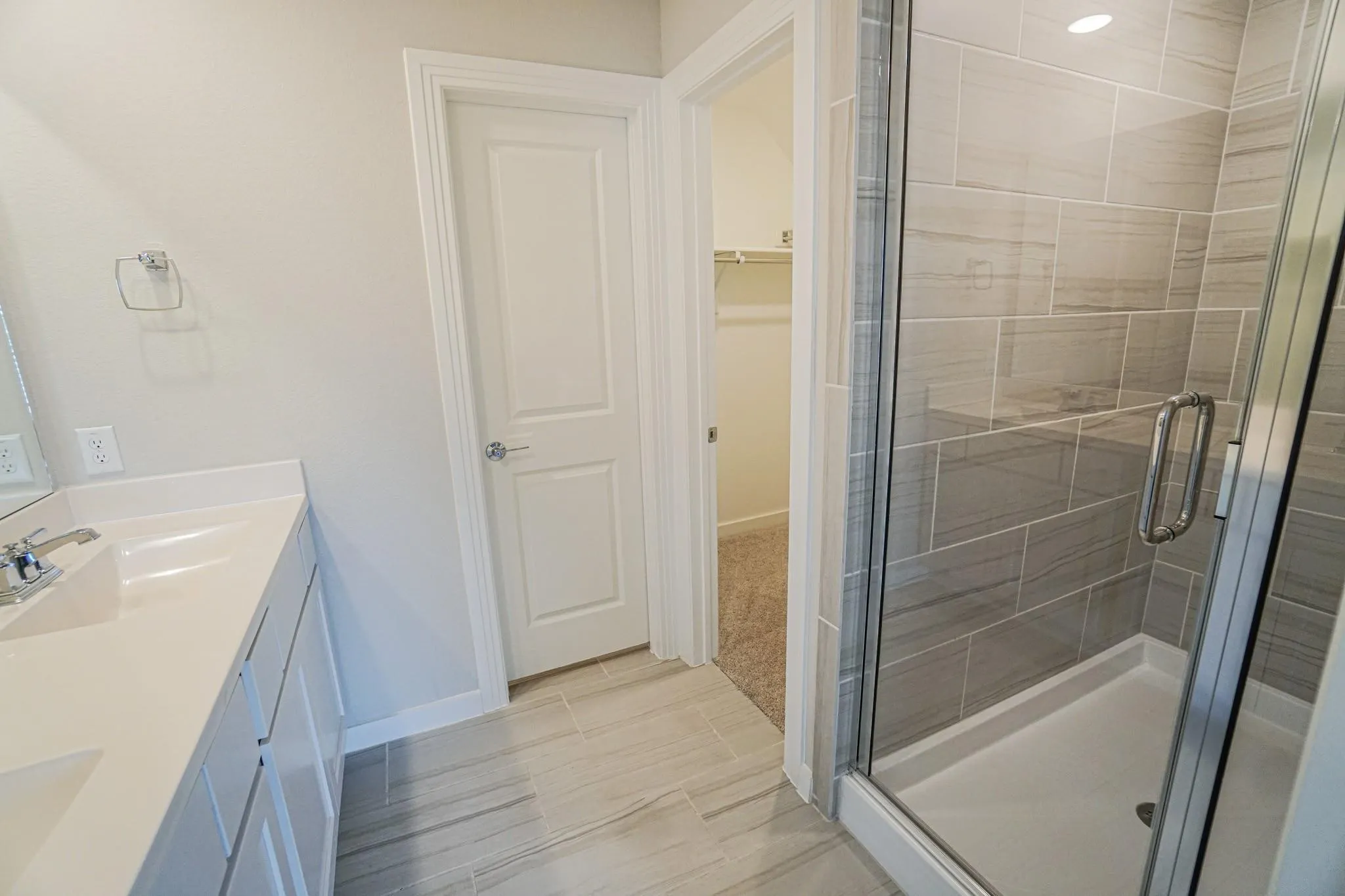 Dual vanity with integrated sinks, glass-enclosed shower with tiled walls, and light-toned tile flooring