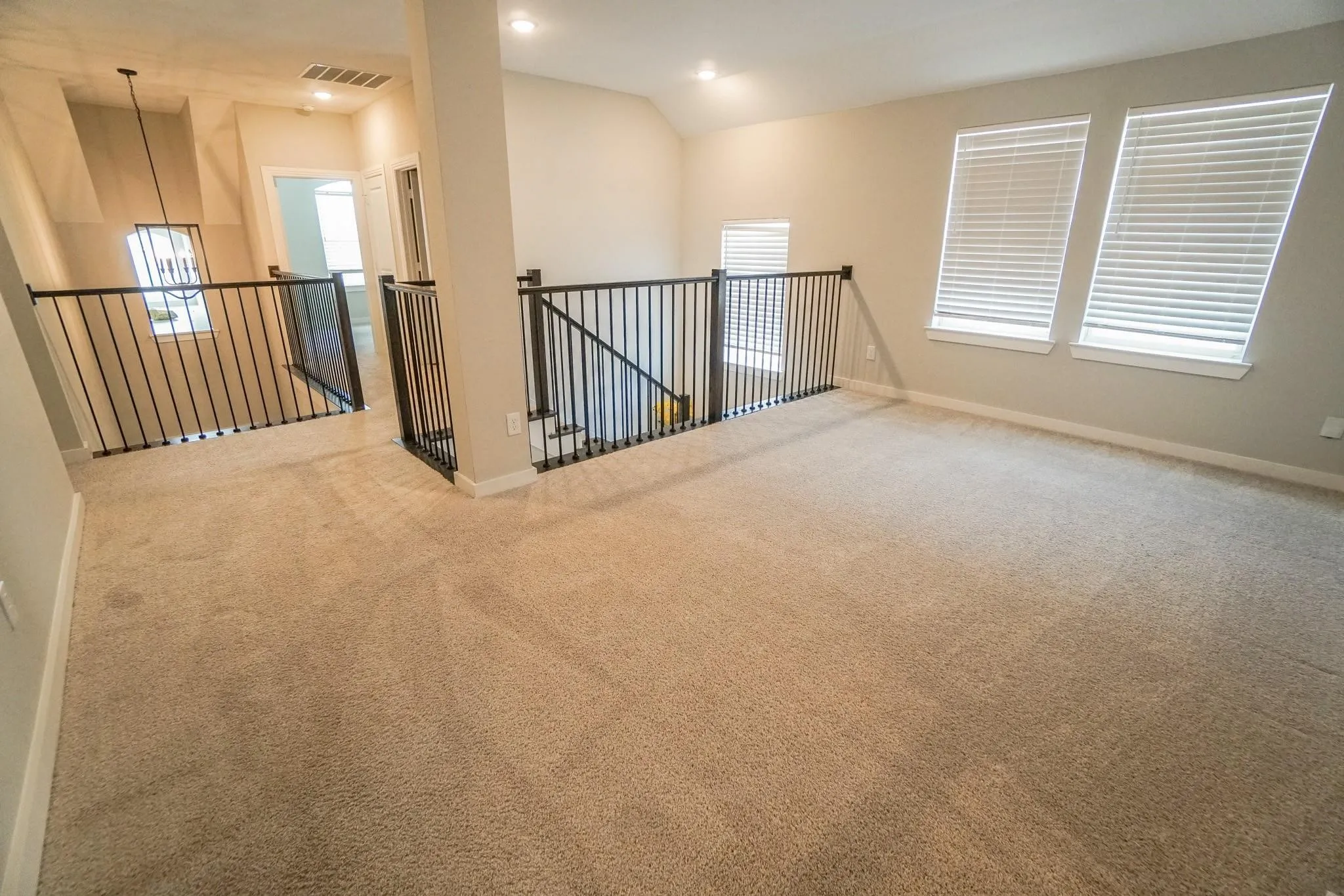 Carpeted loft area with recessed lighting, two windows with blinds, and black metal balusters