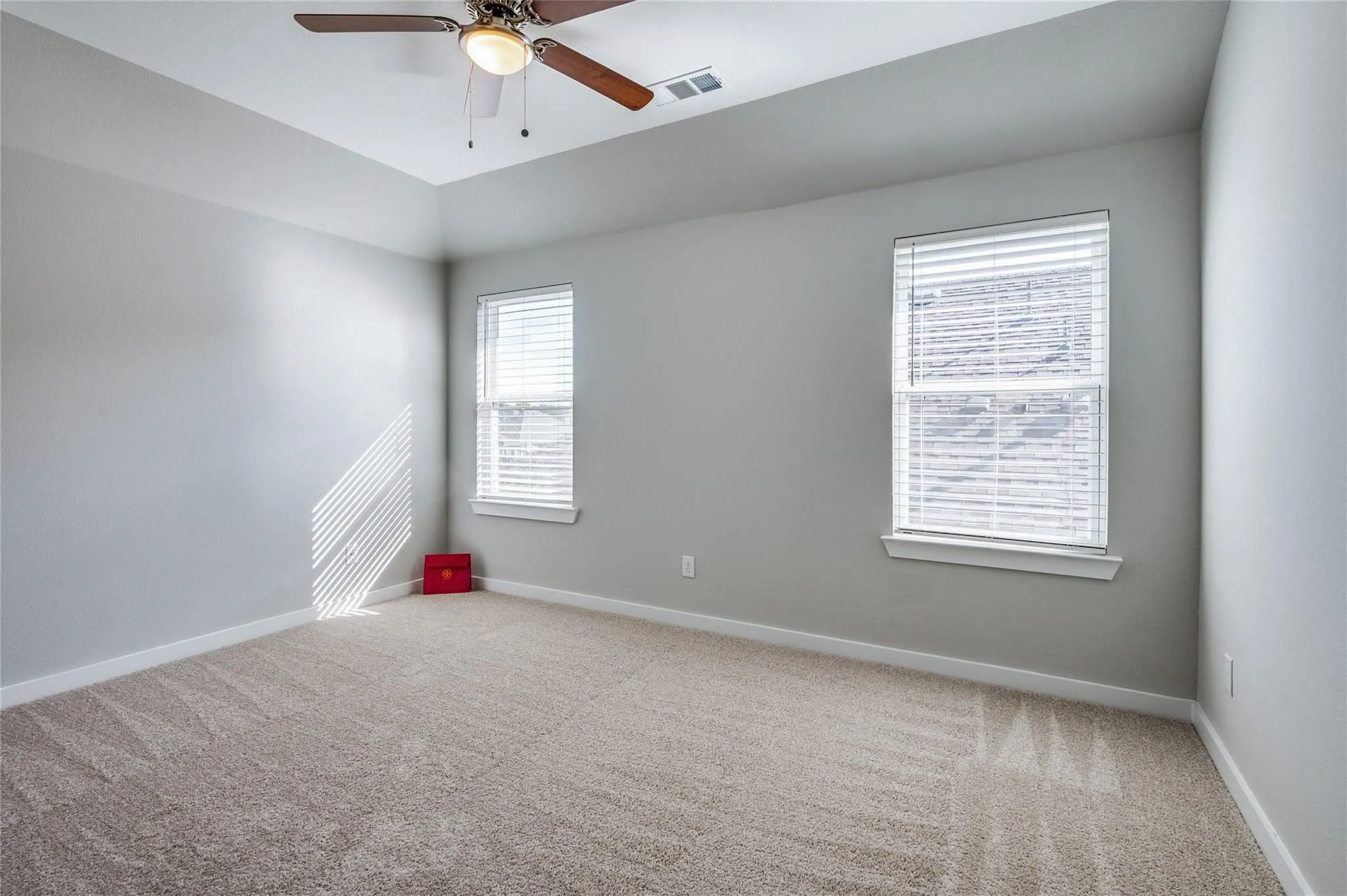 Tray ceiling with a ceiling fan, two windows with blinds, and neutral carpeting