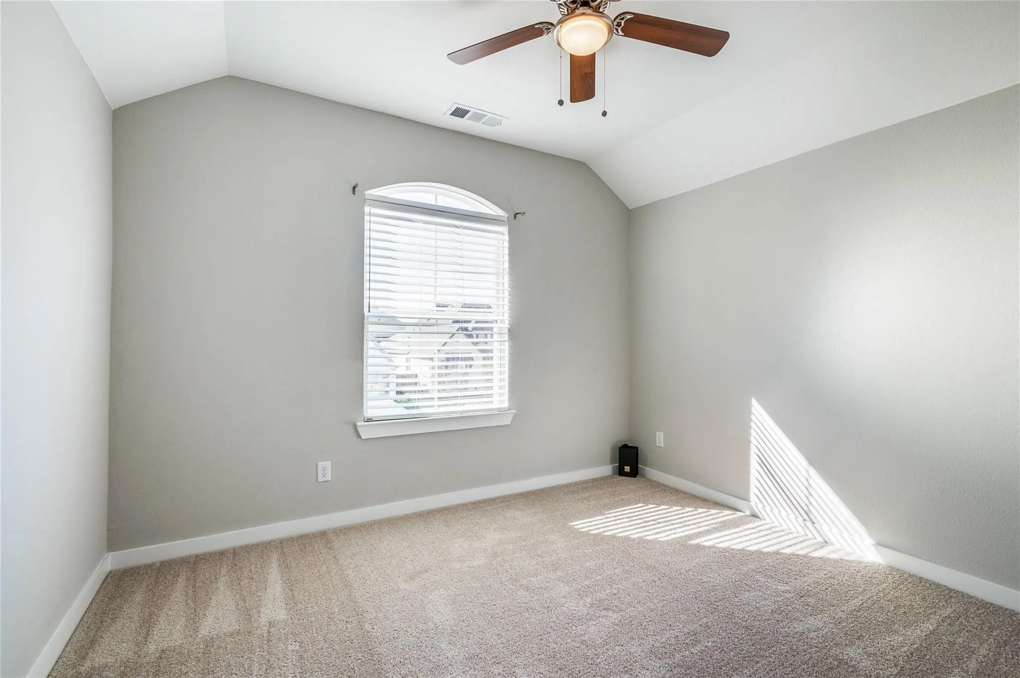 Vaulted ceiling, arched window, ceiling fan with integrated lighting, wall-to-wall carpeting, and neutral paint finishes