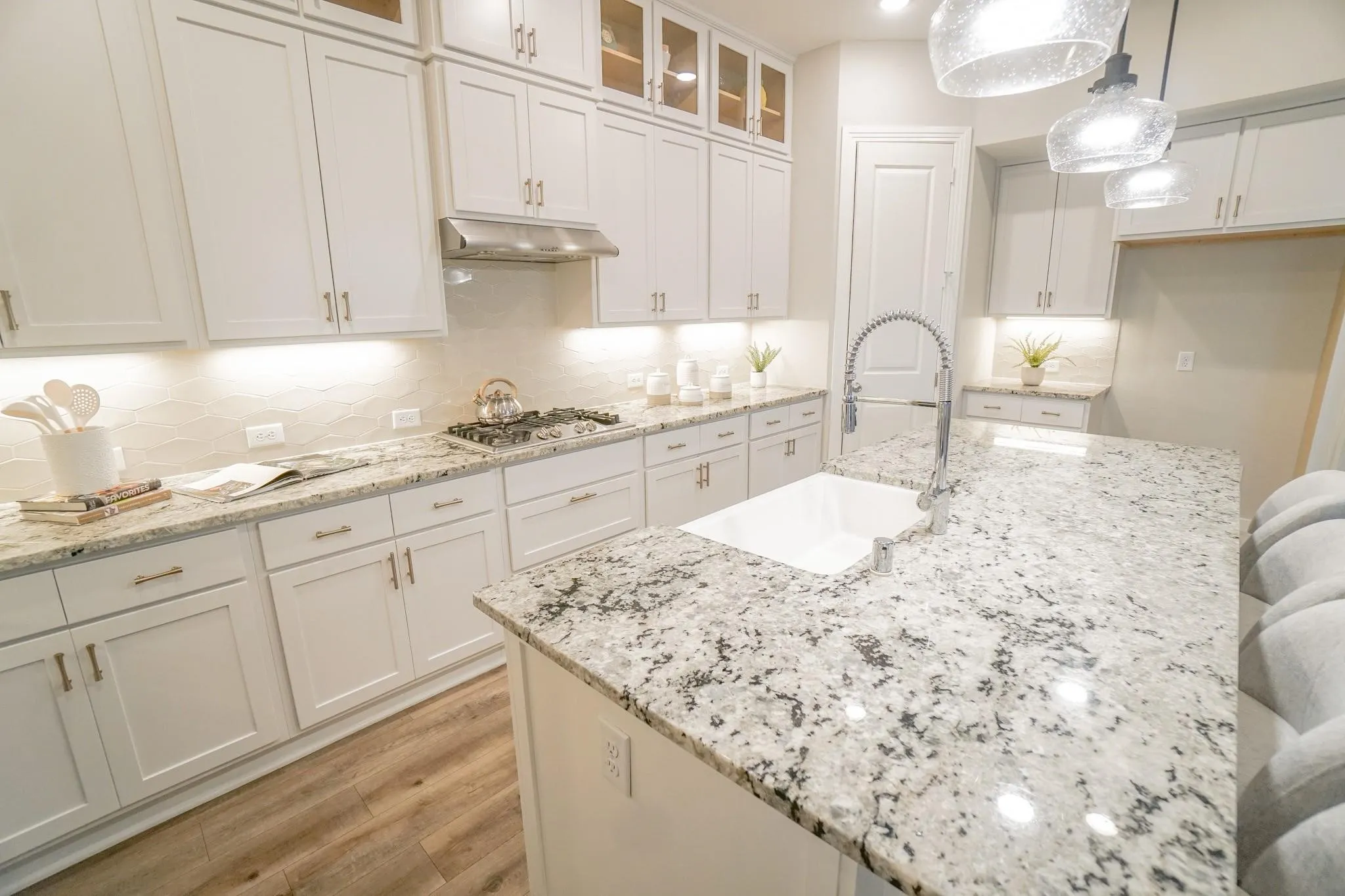 Kitchen featuring white cabinetry, stone countertops, wood-finish flooring, a built-in range, and a large kitchen island with an undermount sink