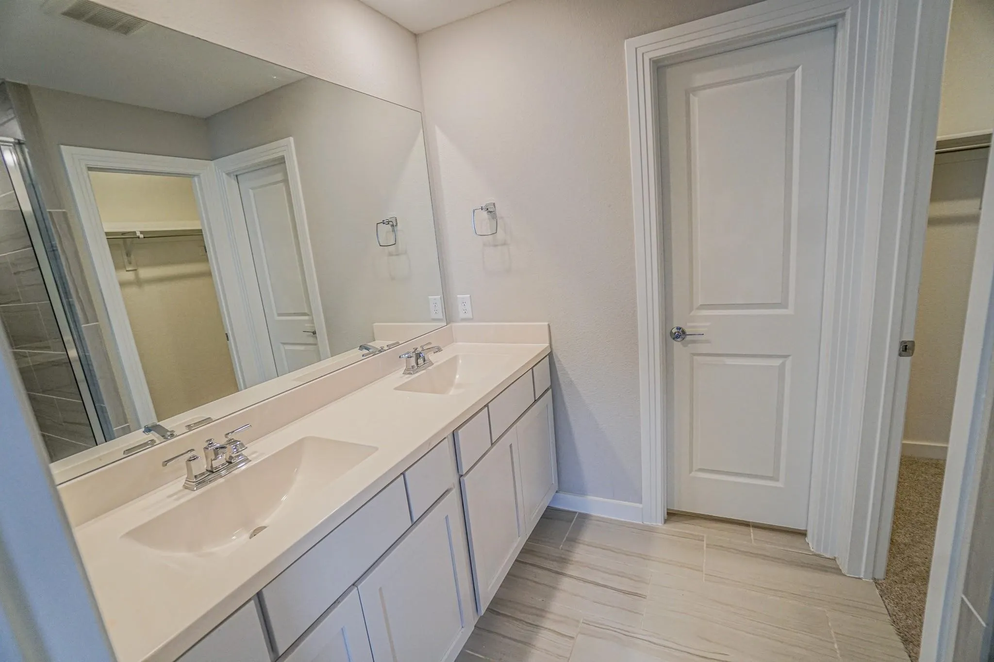 Double vanity with undermount sinks and chrome fixtures, expansive mirror, wood-finish flooring, and white paneled cabinetry