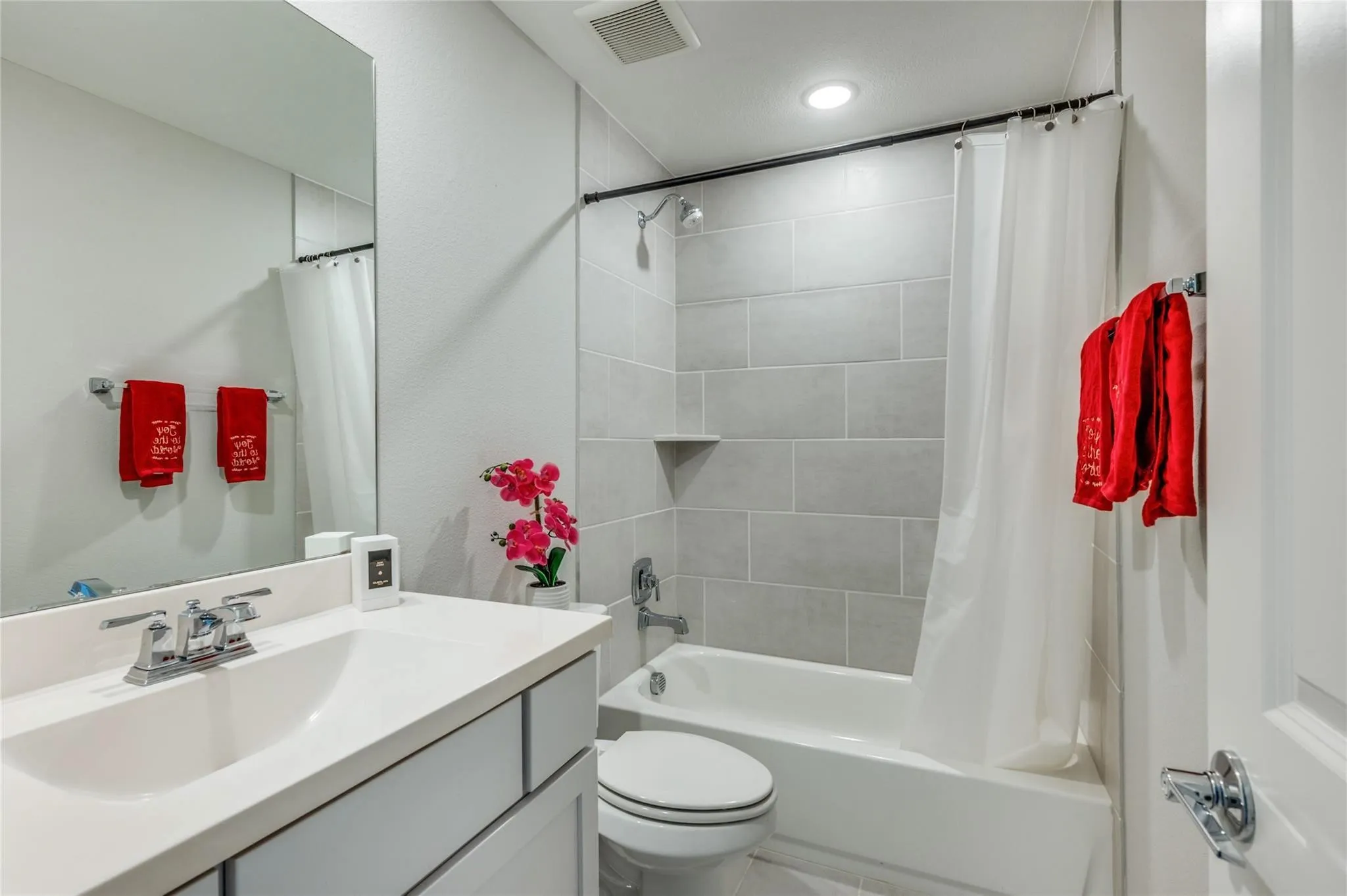 Full-size mirror, single vanity with integrated sink, chrome faucet, tile shower surround, and built-in tub