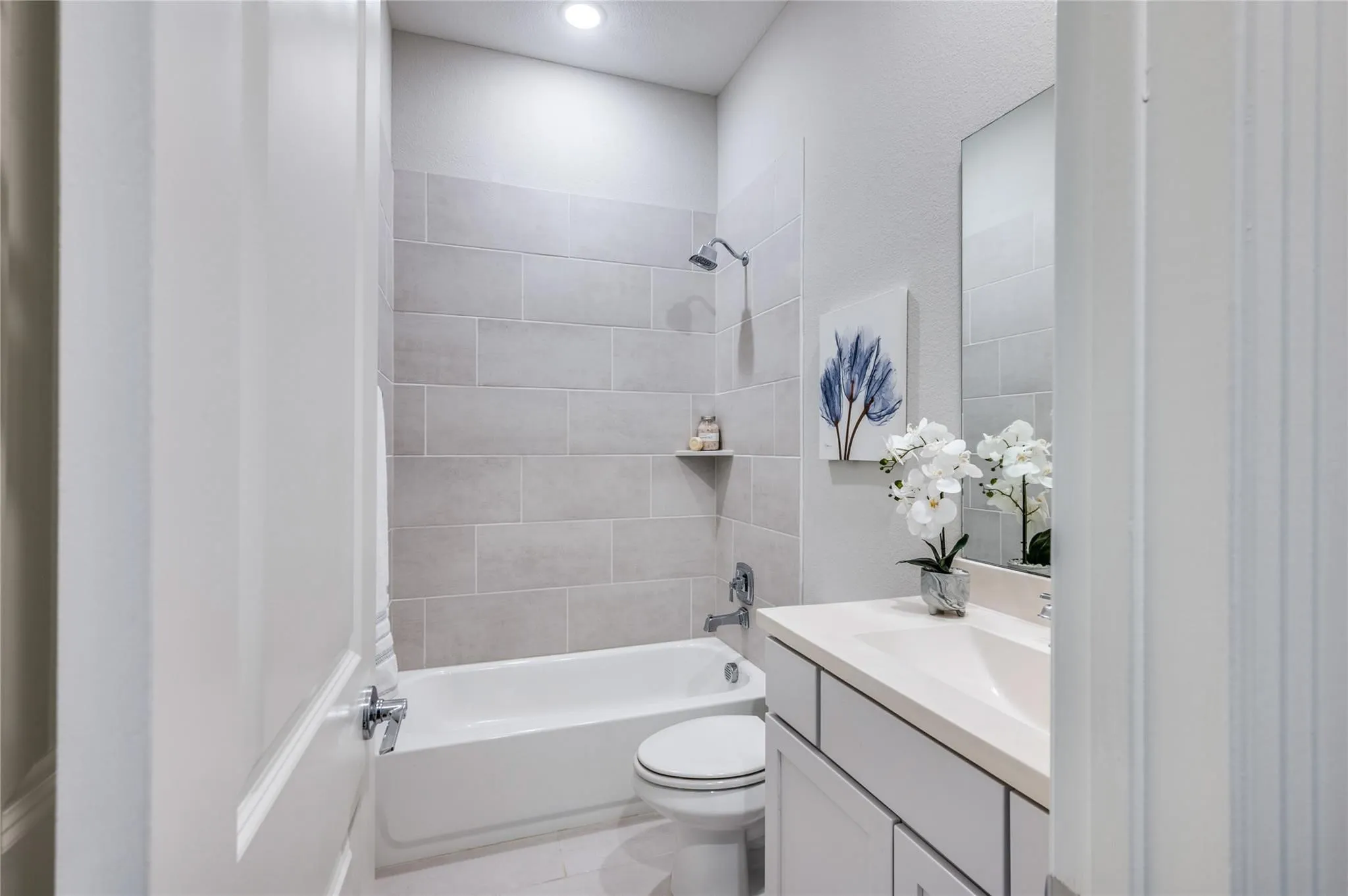 Sleek bathroom featuring a built-in tub with shower, subway tile surround, recessed lighting, and a vanity with an integrated sink