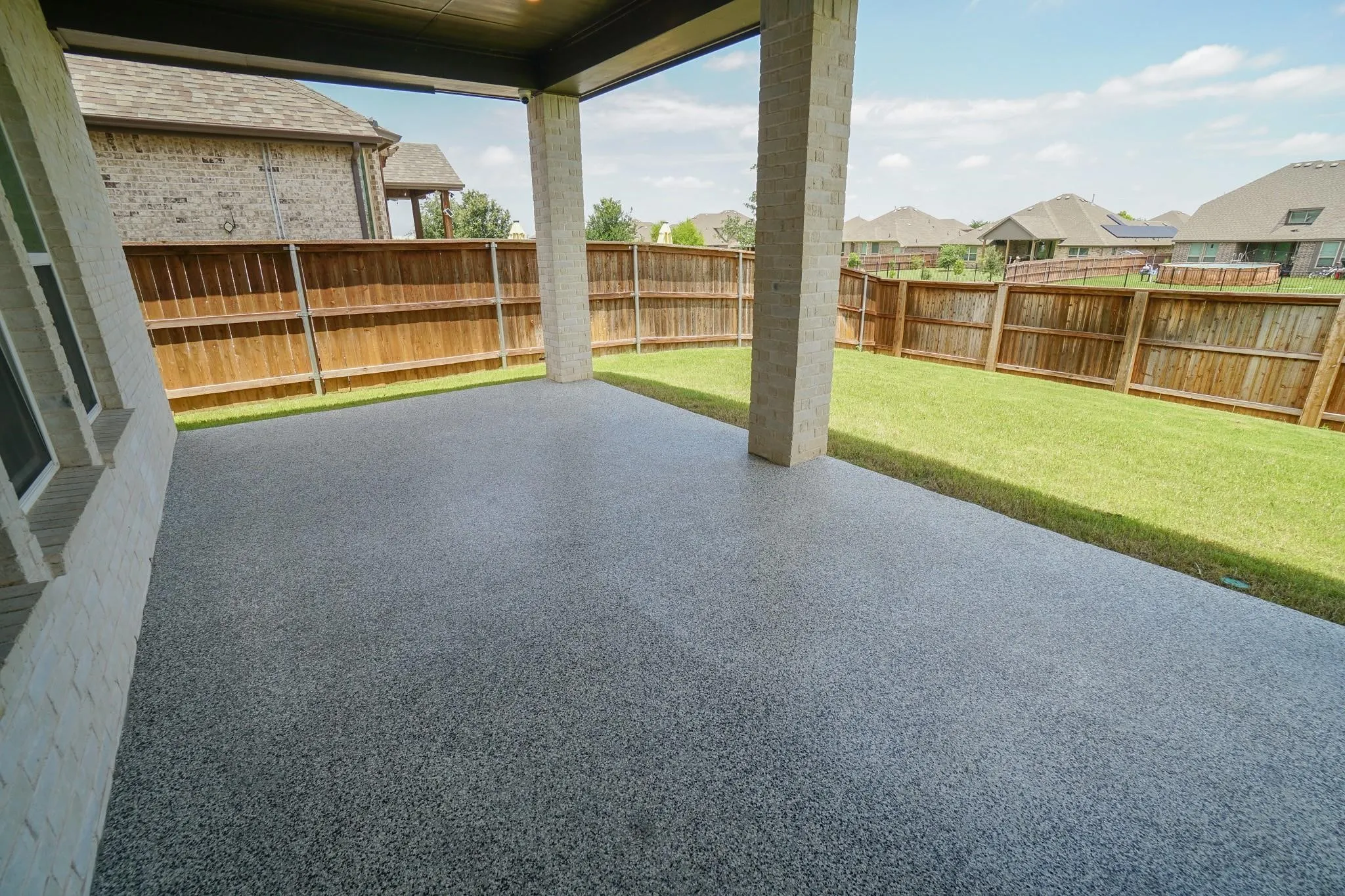 Covered patio with speckled epoxy flooring, brick support columns, and a private fenced yard with a manicured lawn
